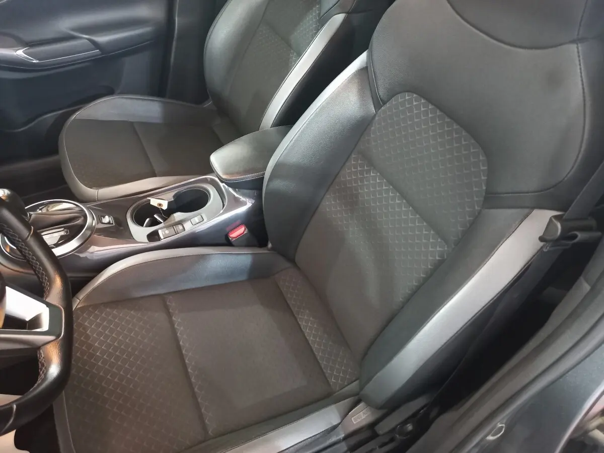 Vue intérieure côté conducteur du Nissan Juke Hybrid 143 Business+ 2023, sièges tissu gris avec accoudoir central cuir.