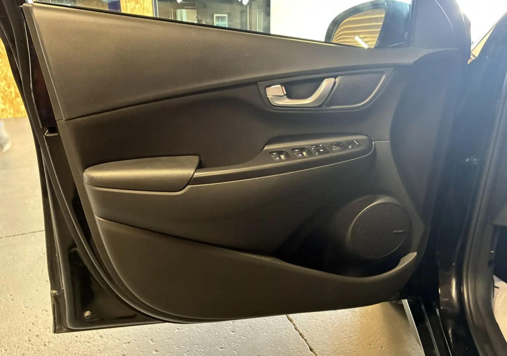 Vue rapprochée de la porte avant gauche noire du Hyundai Kona 2023, avec commandes électriques et haut-parleur Bose intégré.