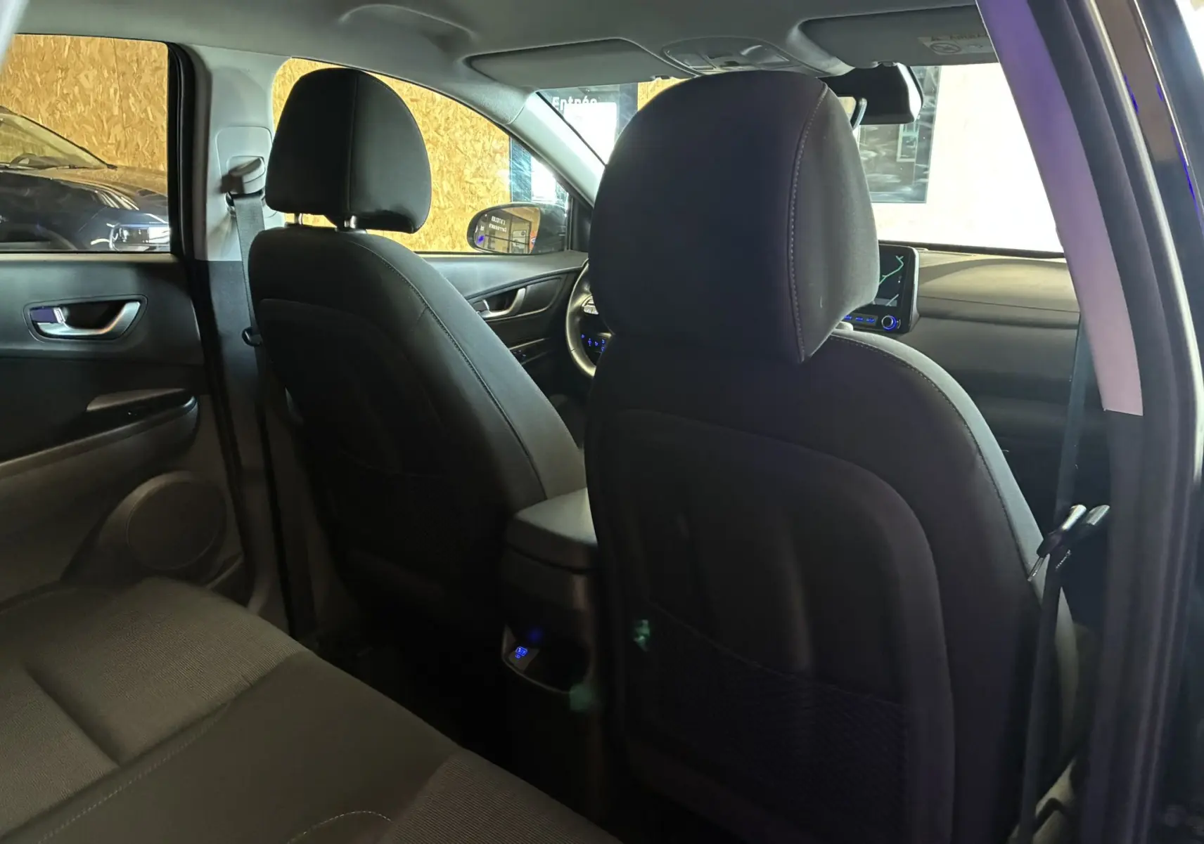 Vue intérieure arrière du Hyundai Kona 2023 noir, montrant les sièges avant en tissu noir et la console centrale.