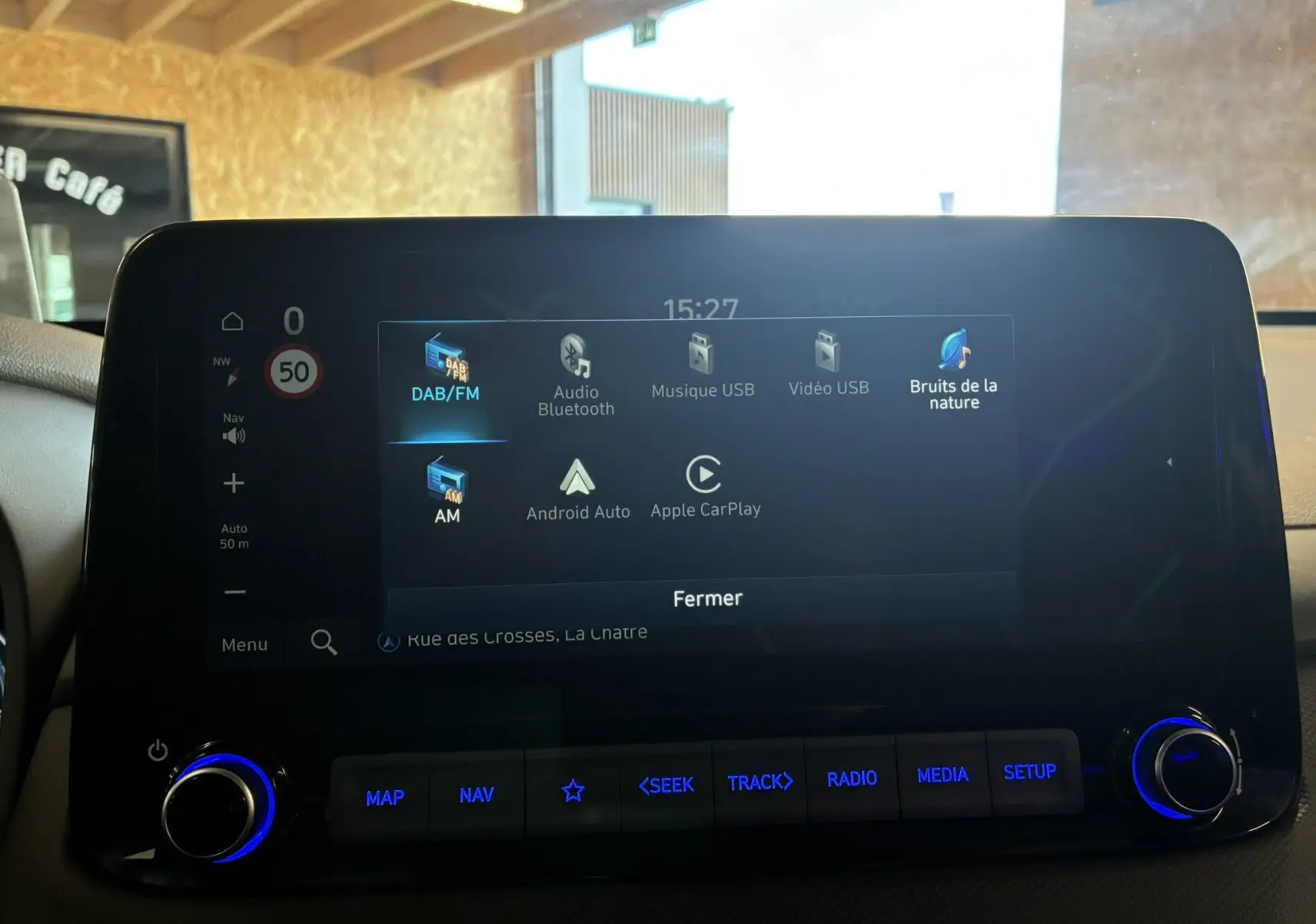 Écran tactile central du Hyundai Kona 2023 montrant les options multimédia avec éclairage bleu des boutons en dessous.