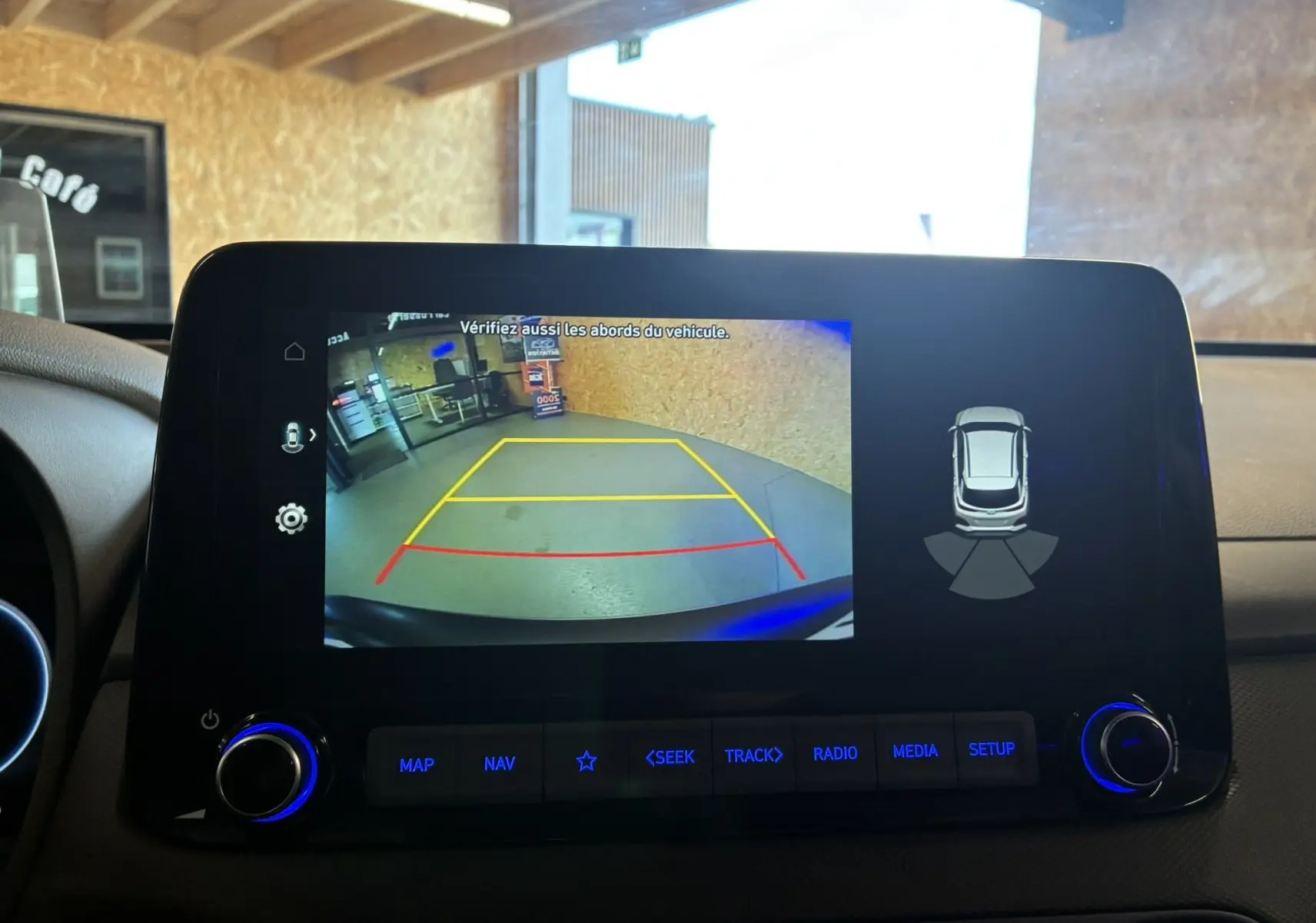 Écran multimédia du Hyundai Kona noir 2023 montrant la caméra de recul avec lignes de guidage colorées en intérieur.