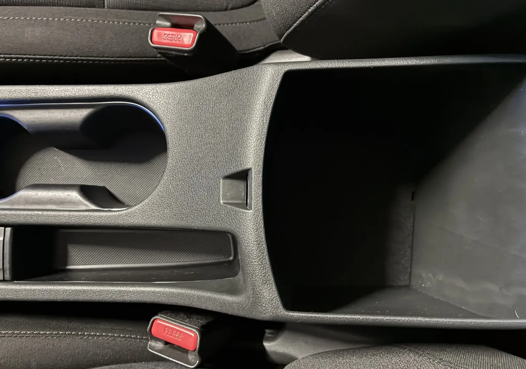 Vue rapprochée de la console centrale noire avec porte-gobelets et rangement du Hyundai Kona 2023 intérieur tissu noir.