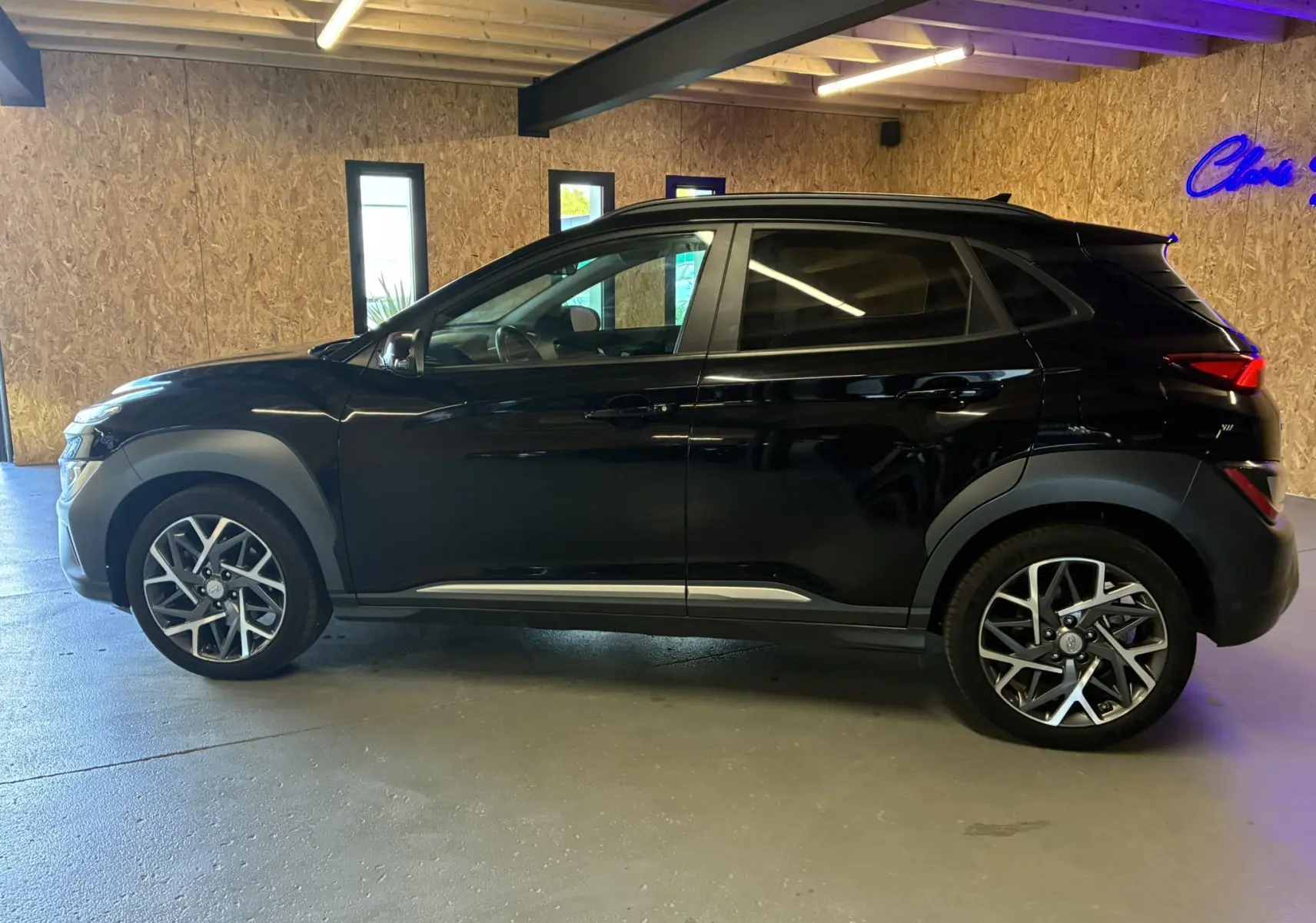 Hyundai Kona 2023 noir en vue profil côté gauche, soulignant ses jantes alliage et ses protections noires sur les passages de roue.