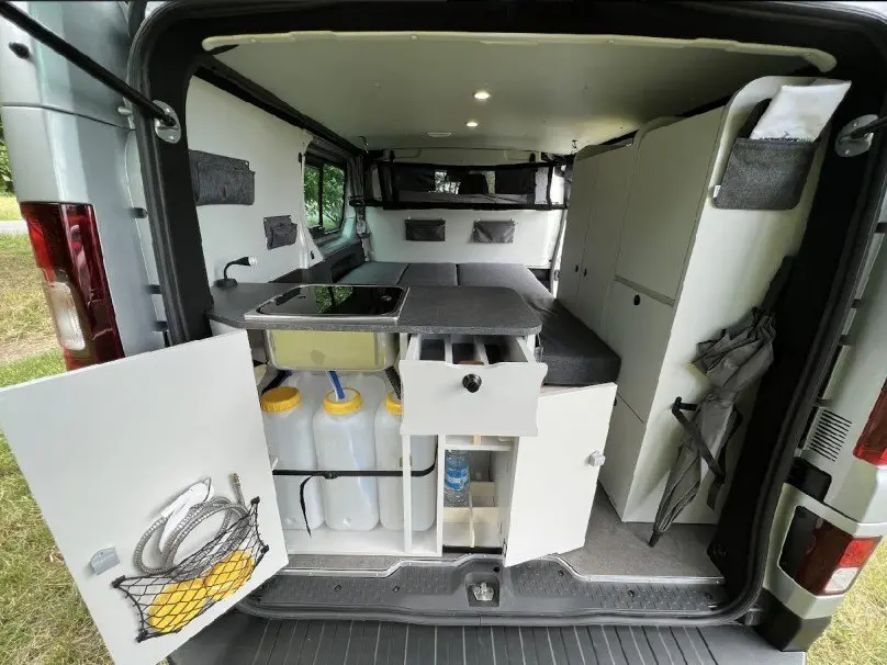 Vue arrière intérieure du Renault Trafic Fourgon gris 2025 aménagé avec kitchenette, rangements et couchage.
