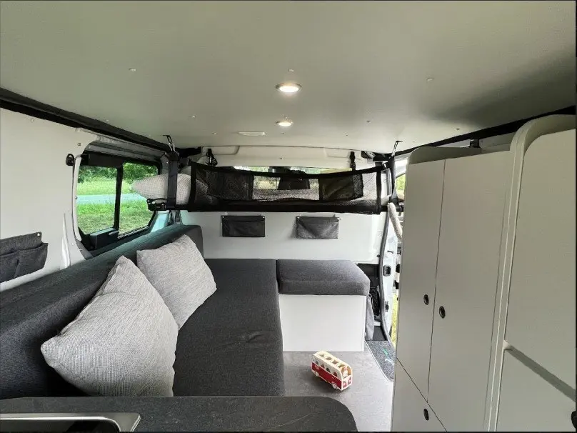 Intérieur du Renault Trafic Fourgon aménagé, vue de côté droit montrant banquette grise et rangements blancs.