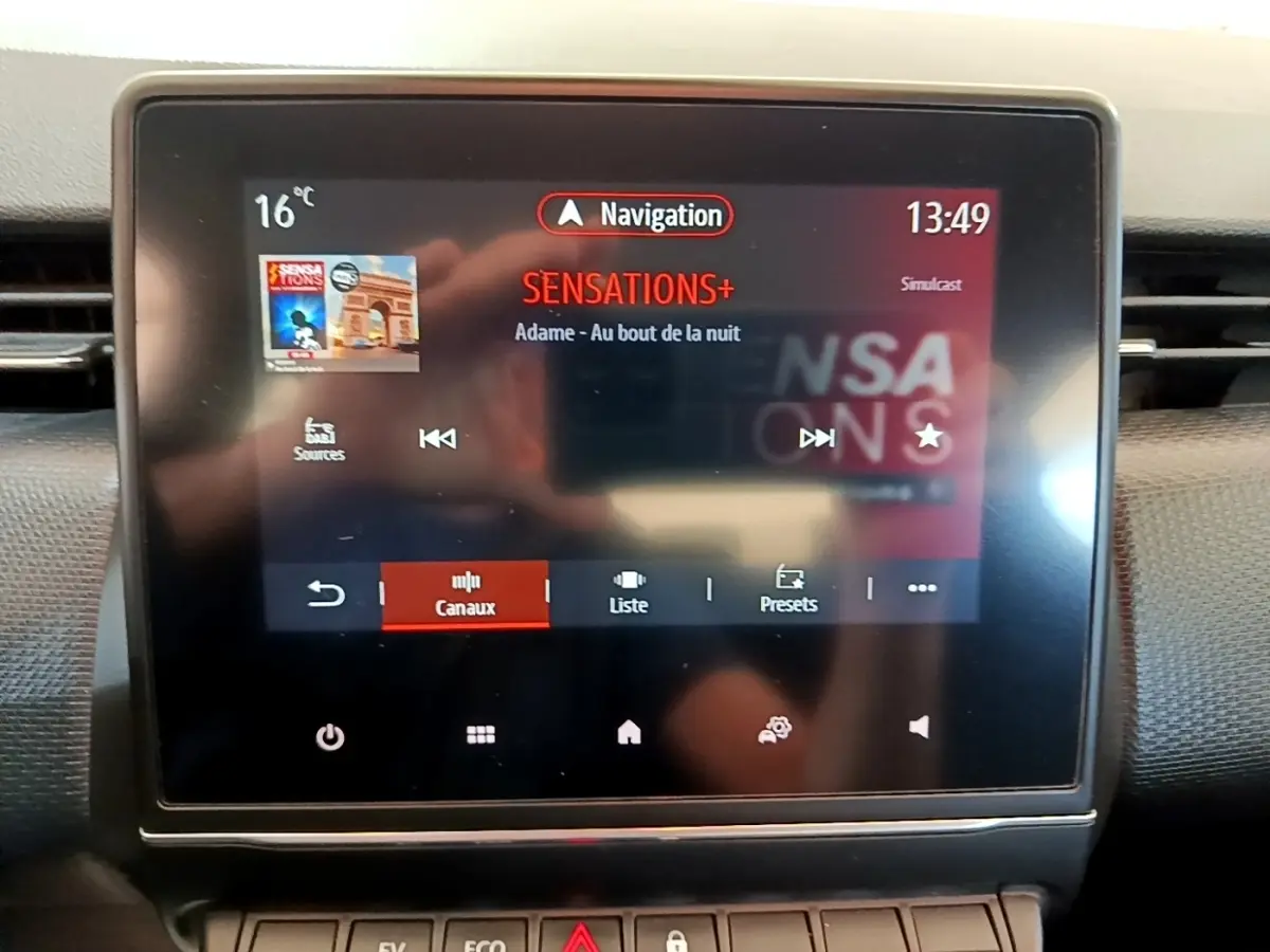 Écran tactile central de la Renault Clio Business E-Tech hybride bleu, affichant la radio Sensations+ en mode navigation.