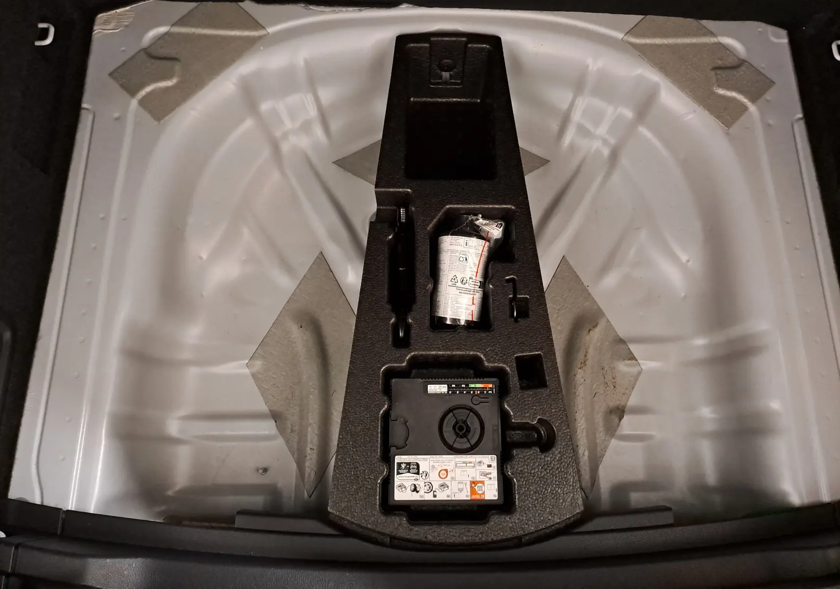 Vue plongeante sur le coffre du Skoda Karoq blanc Lune, montrant le rangement pour roue de secours et kit de réparation.