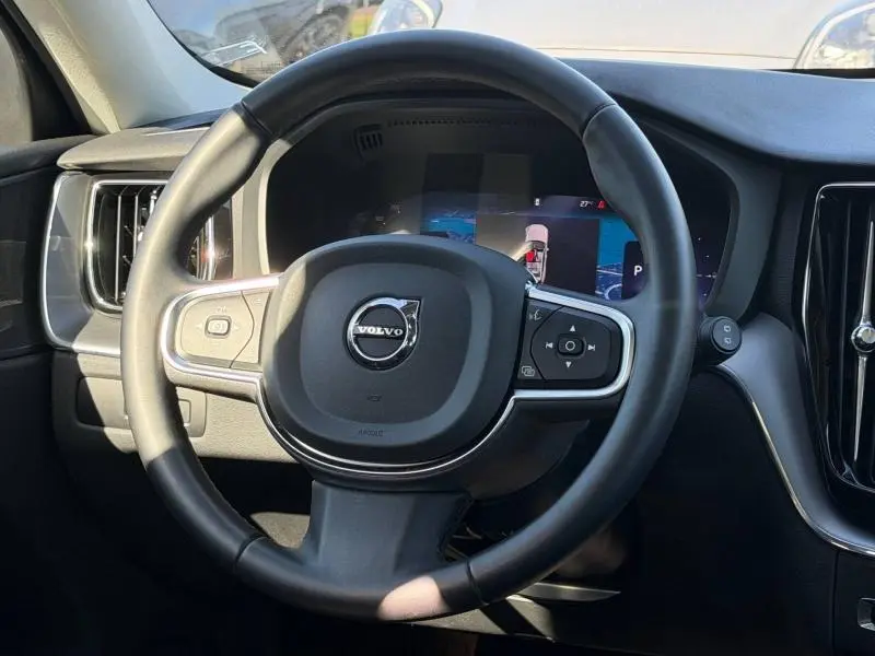 Vue rapprochée du volant cuir noir multifonction du Volvo XC60 2024 avec tableau de bord digital en arrière-plan.