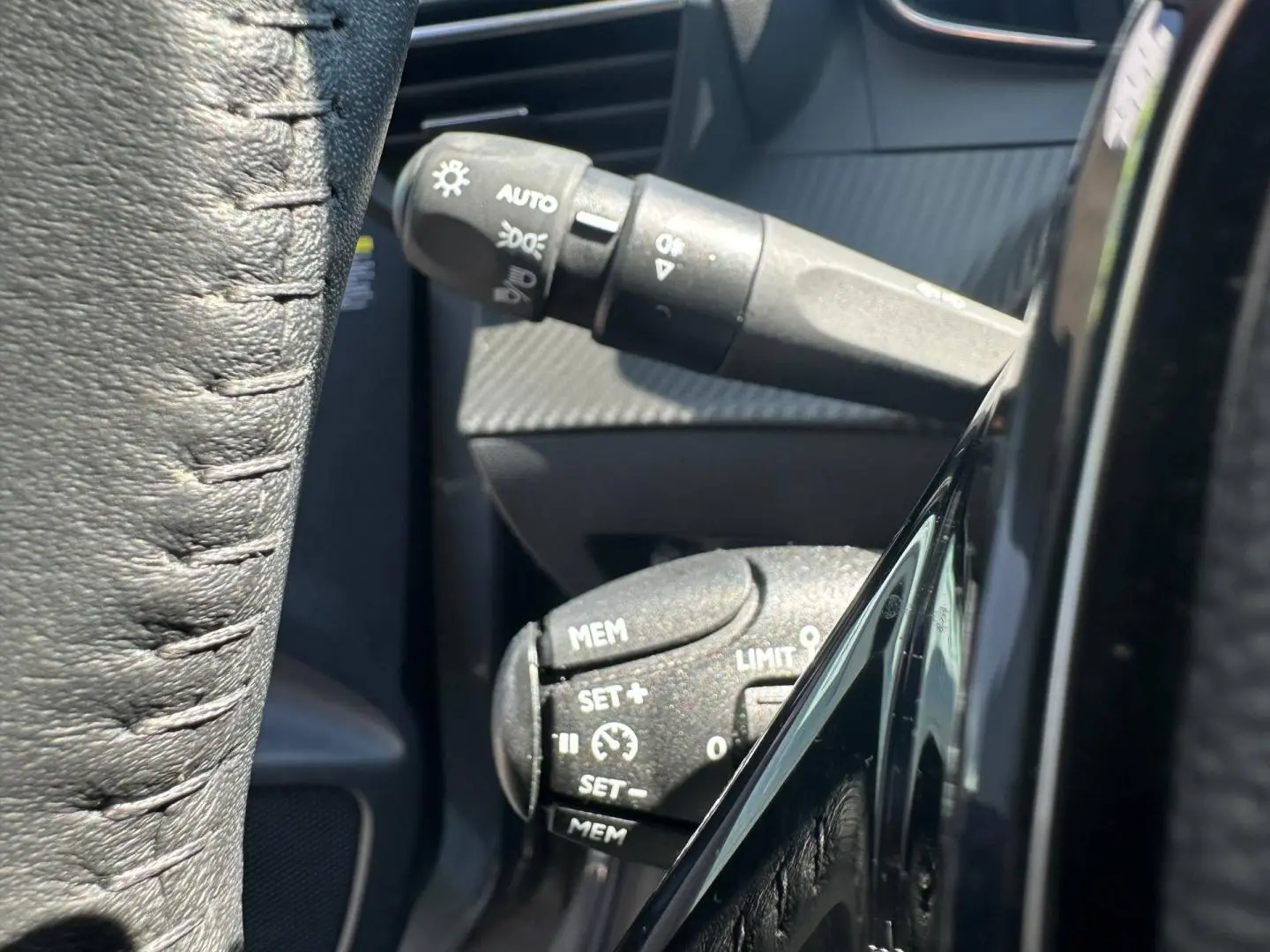 Gros plan sur les commandes au volant de la Peugeot 208 1.2 100ch Allure, avec détails en noir mat et cuir noir.