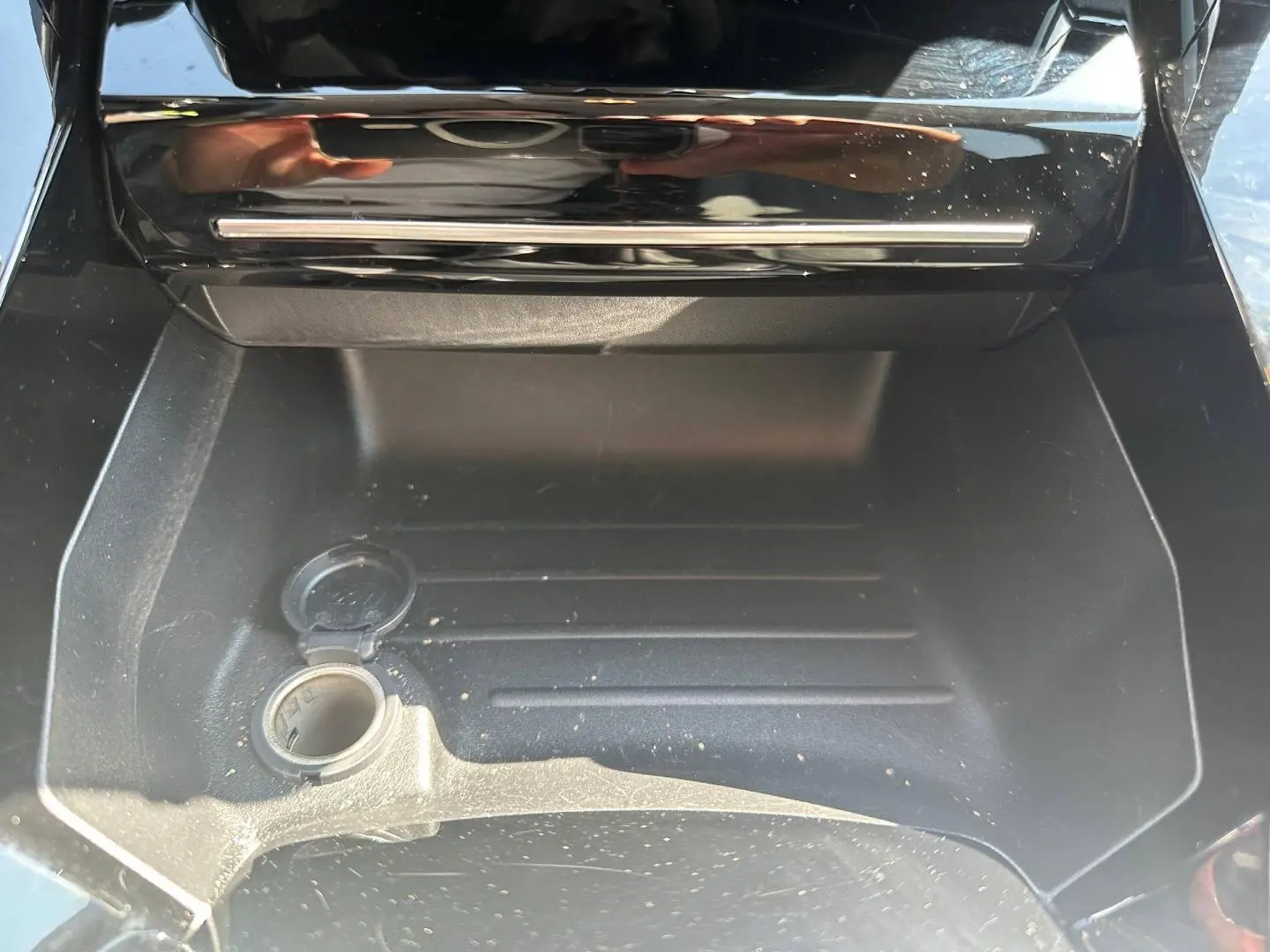 Vue rapprochée de la prise 12V ouverte dans le rangement central avant d'une Peugeot 208 gris Selenium.