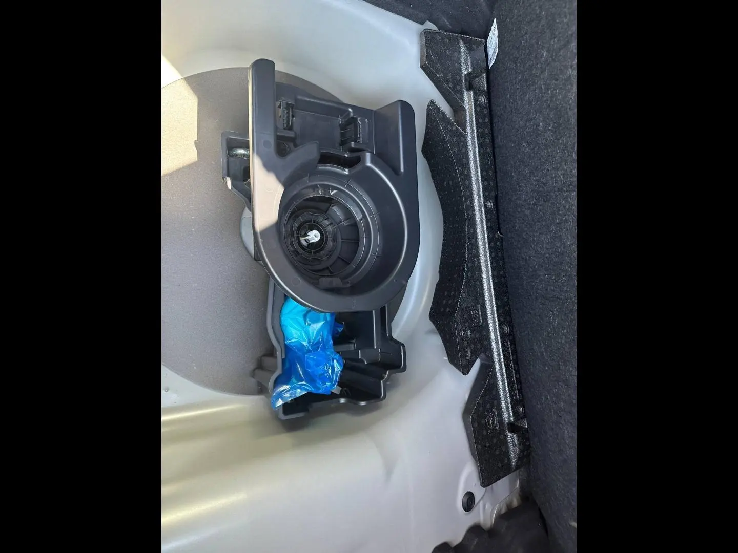 Gros plan sur le rangement sous le plancher du coffre de la Peugeot 208 gris Selenium, montrant un support plastique noir.