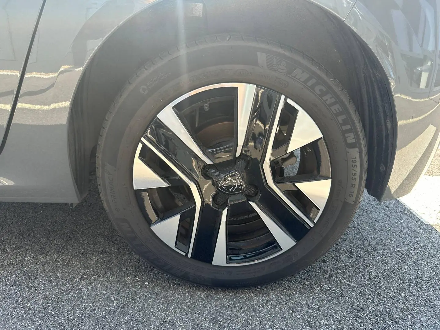 Gros plan sur la jante alu bicolore noire et argentée du côté avant droit d'une Peugeot 208 gris Selenium.