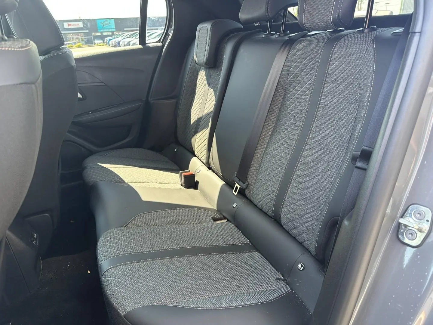 Vue intérieure côté arrière droit montrant la banquette tissu gris avec appuie-têtes et ceintures de sécurité de la Peugeot 208 2025.