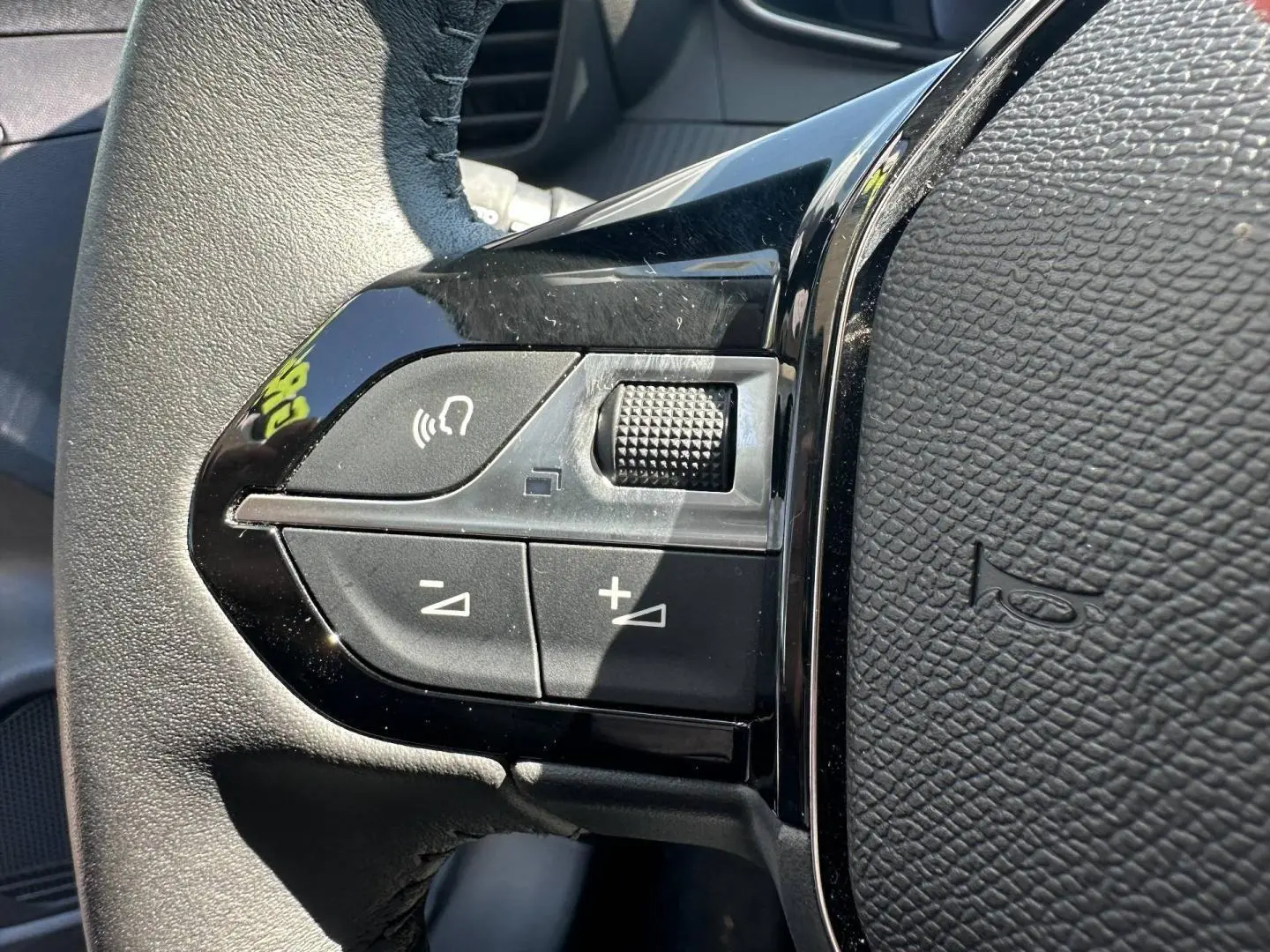 Gros plan sur les commandes noires du volant côté gauche de la Peugeot 208 1.2 100ch Gris Selenium 2025.