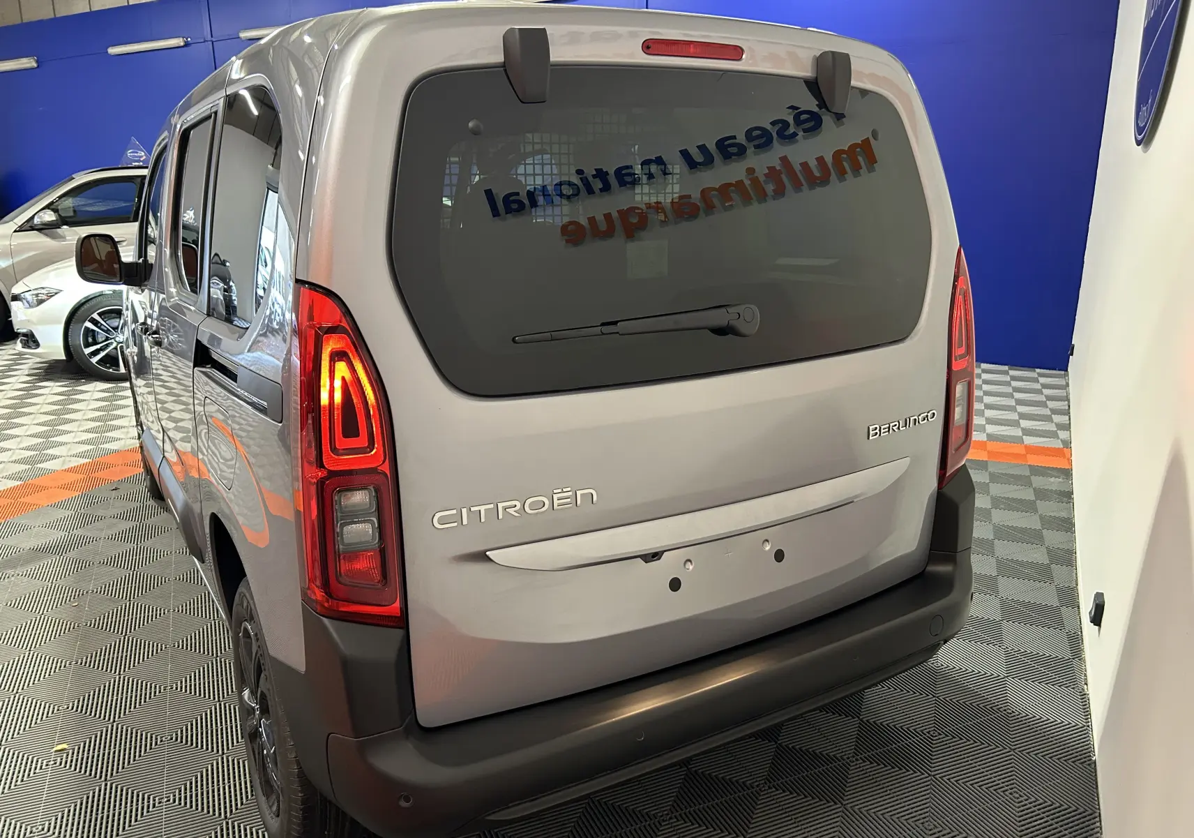 Vue 3/4 arrière du Citroën Berlingo Multispace gris Artense avec feux arrière allumés en intérieur showroom.