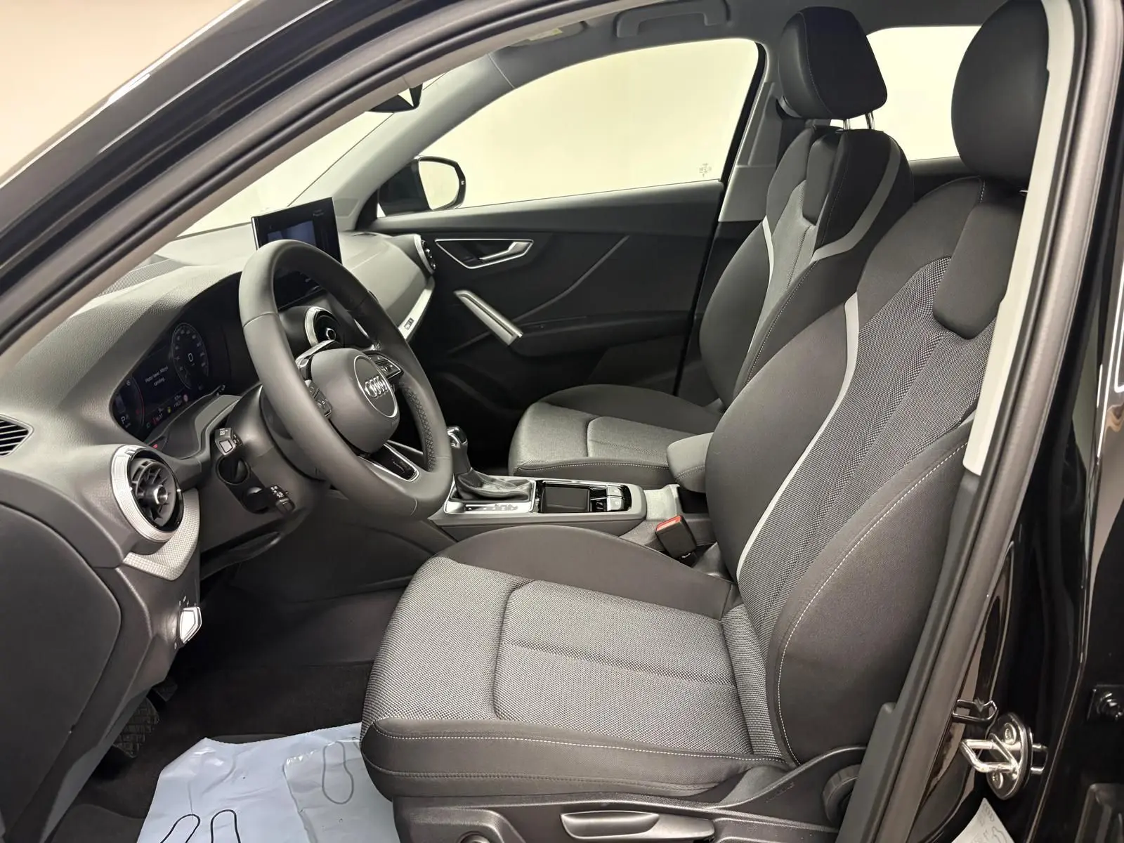 Vue intérieure côté conducteur de l'Audi Q2 35 TFSI S Line 2026 en Noir Mythic, sièges avant en tissu gris et noir.