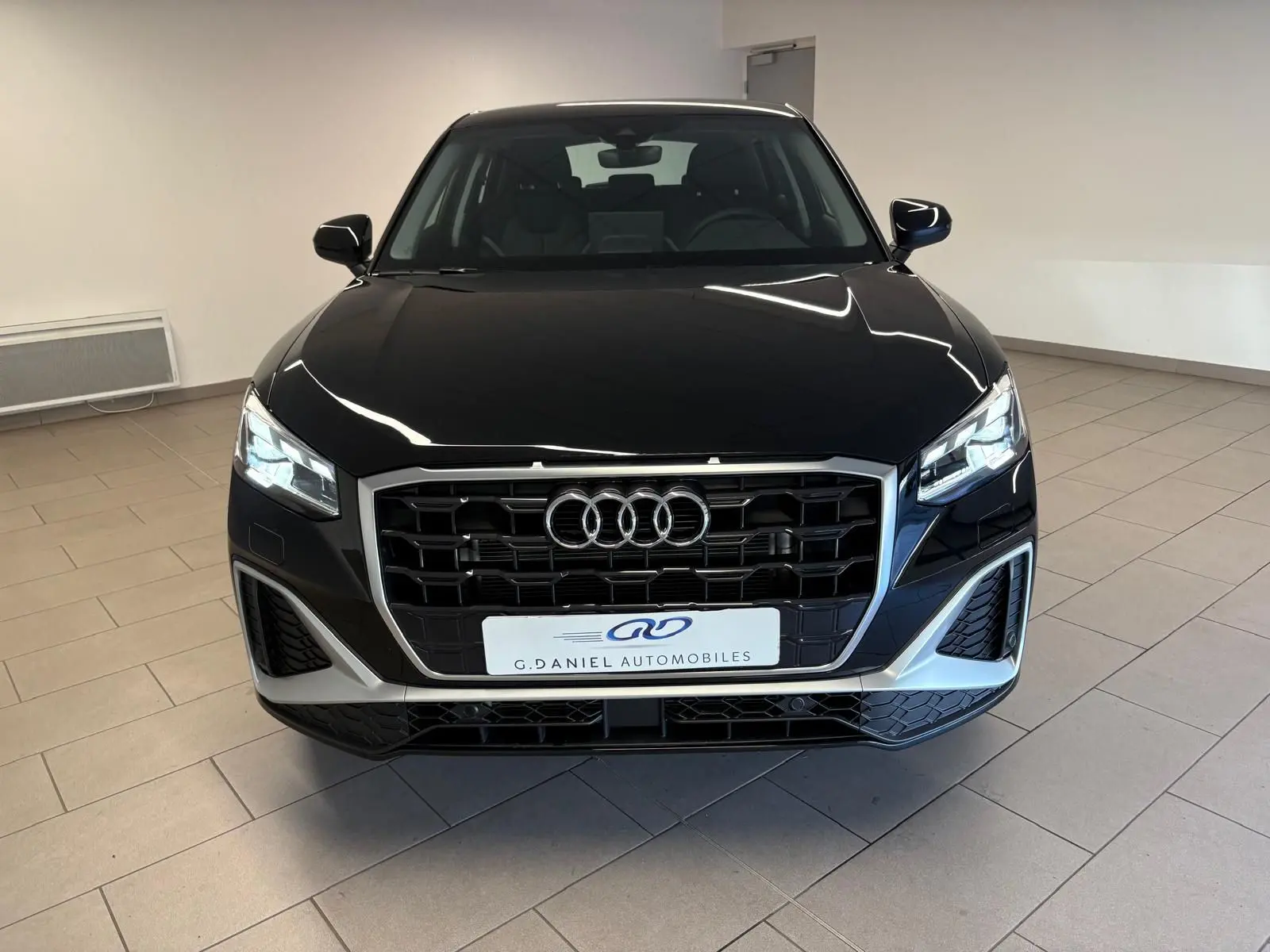 Vue avant d'un Audi Q2 35 TFSI S Line noir mythic avec calandre large et phares LED allumés en intérieur.