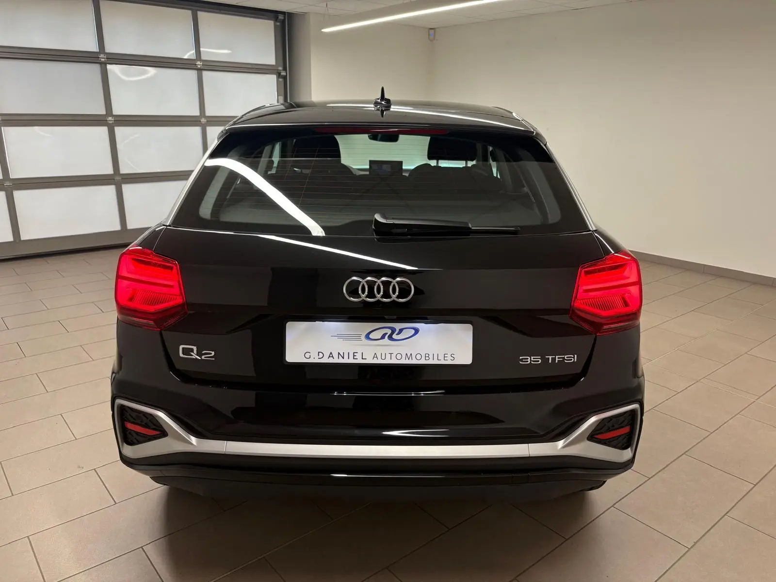 Vue arrière d'un Audi Q2 35 TFSI noir Mythic avec feux rouges allumés dans un showroom intérieur.