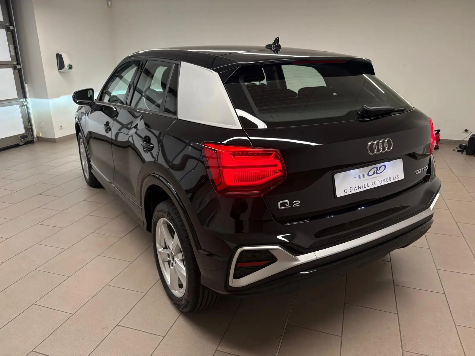 Vue 3/4 arrière droite d'un Audi Q2 35 TFSI S Line noir Mythic avec inserts argentés et feux arrière allumés en intérieur.
