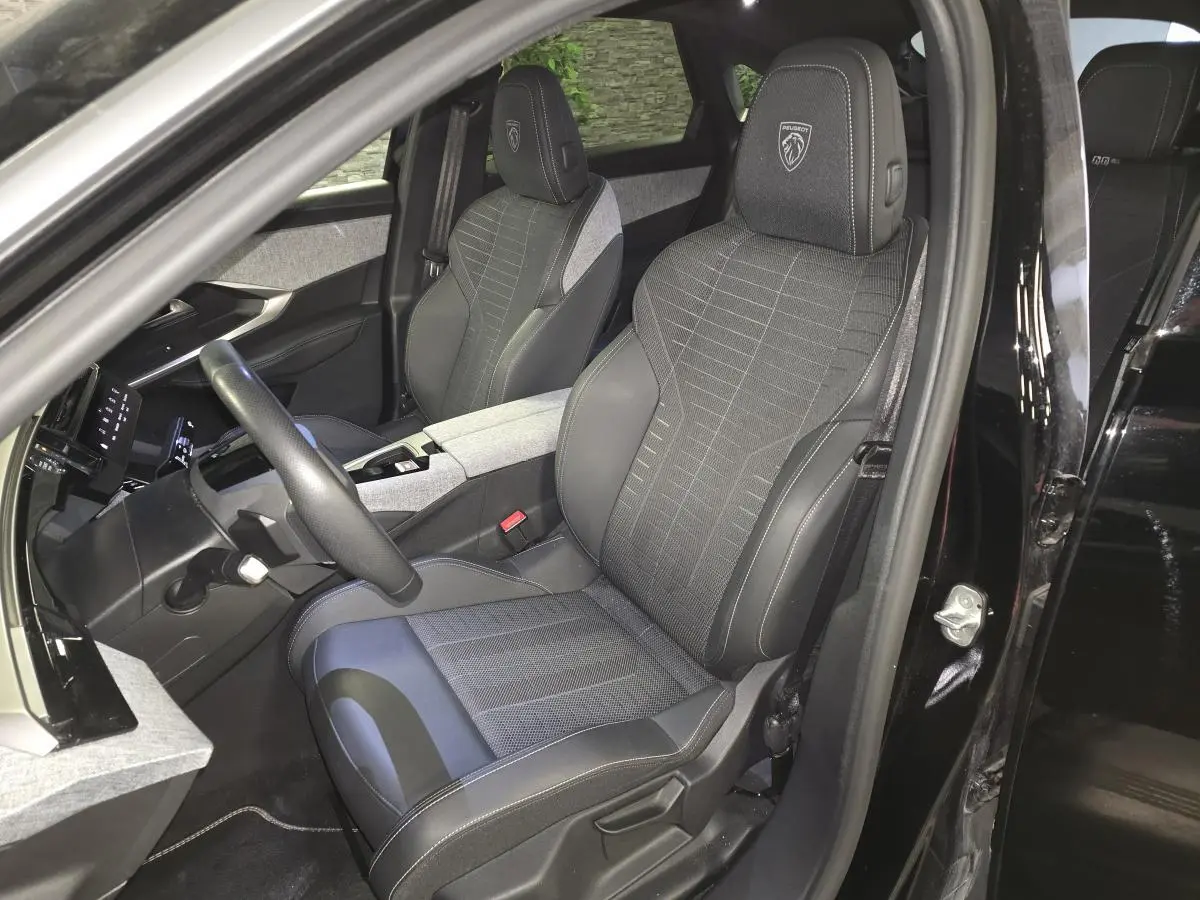 Vue intérieure côté conducteur du Peugeot 3008 Hybrid 2025 noir, sièges tissu et cuir avec logo Peugeot brodé.