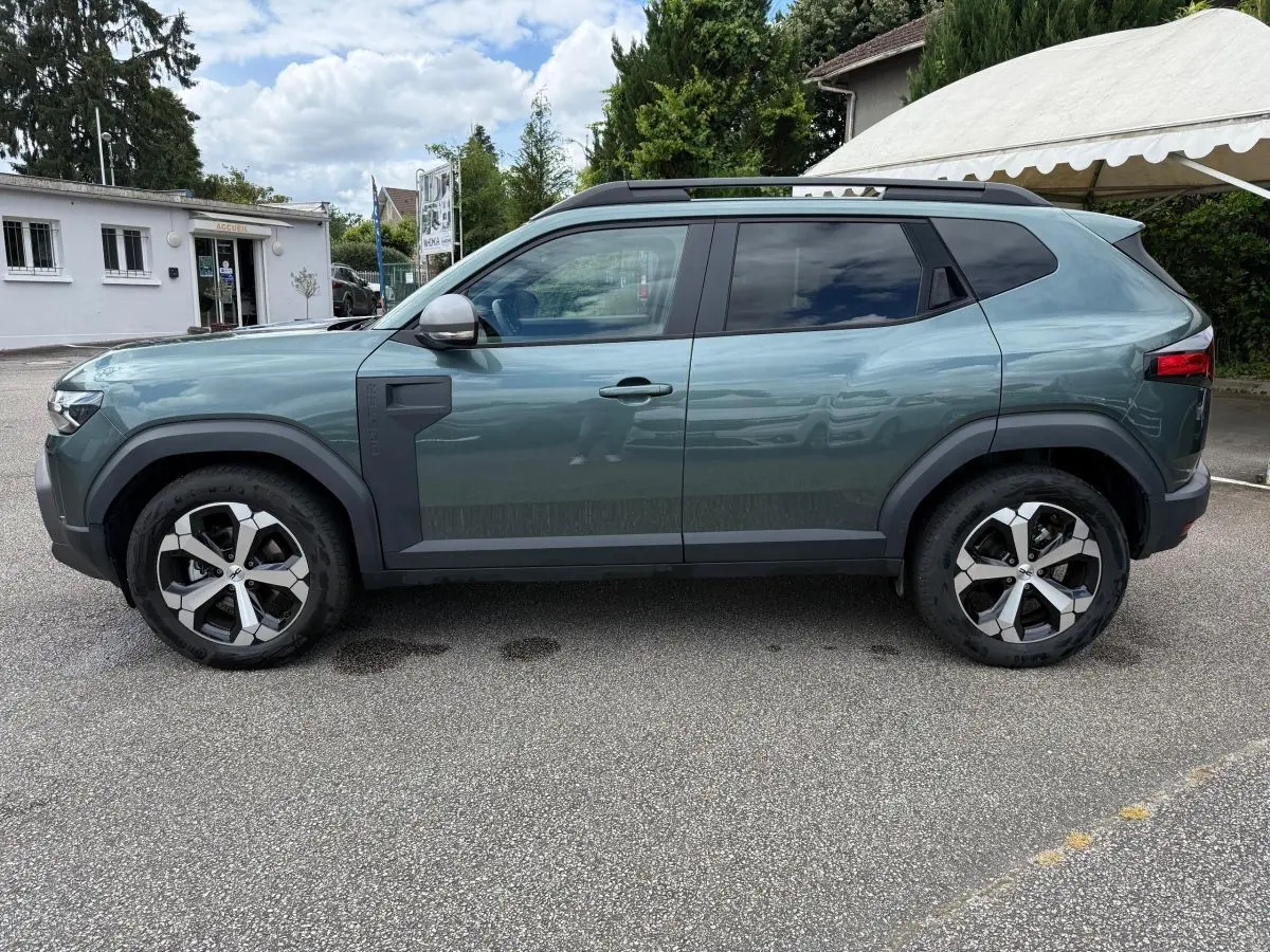 Vue de profil côté gauche du Dacia Duster Hybrid 140 Journey vert cèdre avec jantes alliage et barres de toit noires.