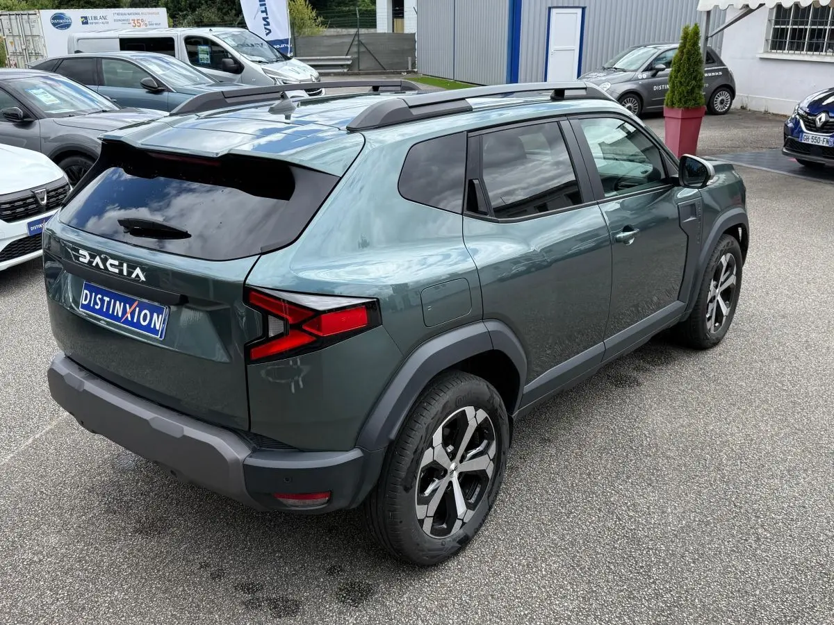 Vue 3/4 arrière droite du Dacia Duster Hybrid 140 Journey vert cèdre avec barres de toit et jantes noires.