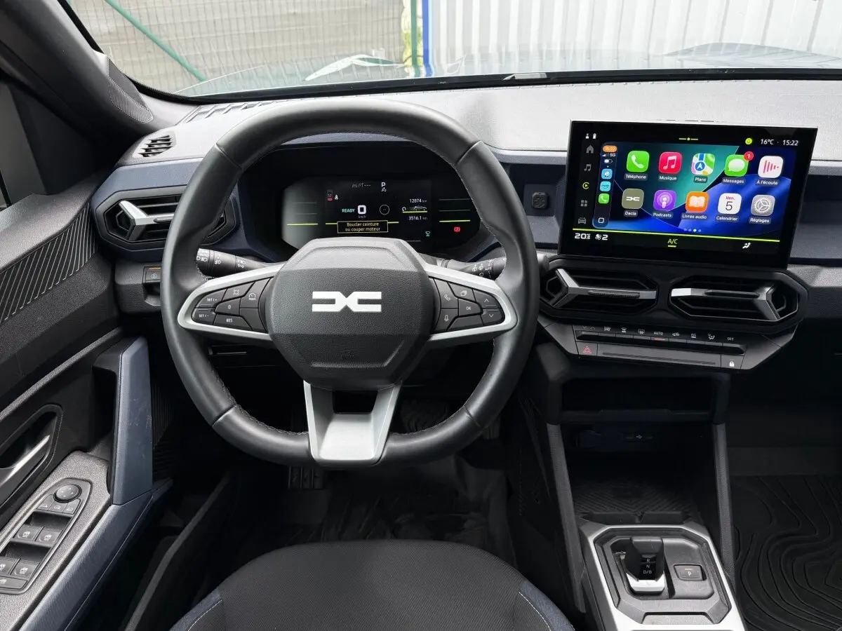 Vue intérieure frontale du tableau de bord du Dacia Duster Hybrid 140 Journey avec écran tactile et volant multifonctions.