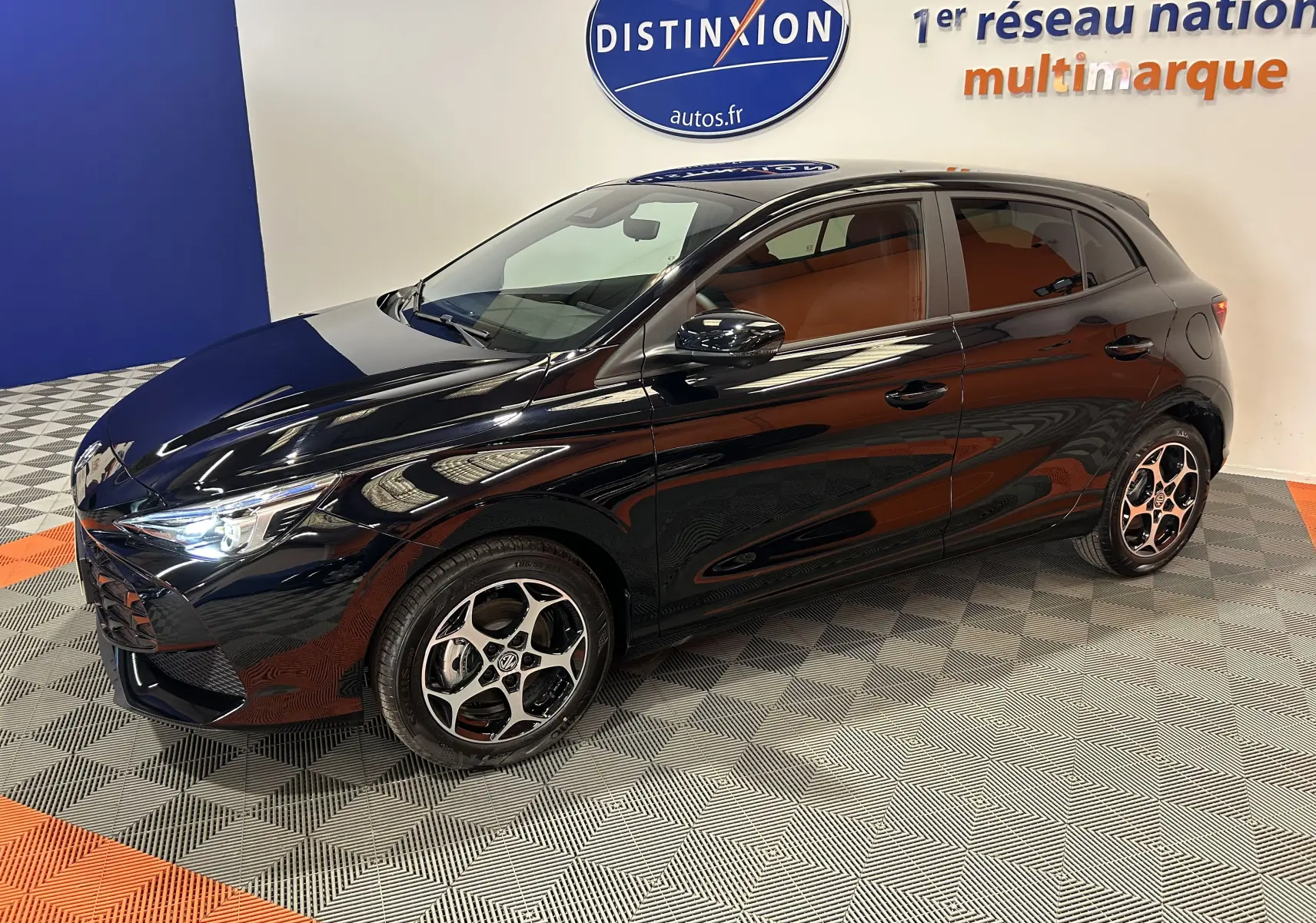Vue 3/4 avant droite de la MG3 Hybrid+ 195 Luxury noire Pebble Black avec jantes alliage et phares allumés en showroom.