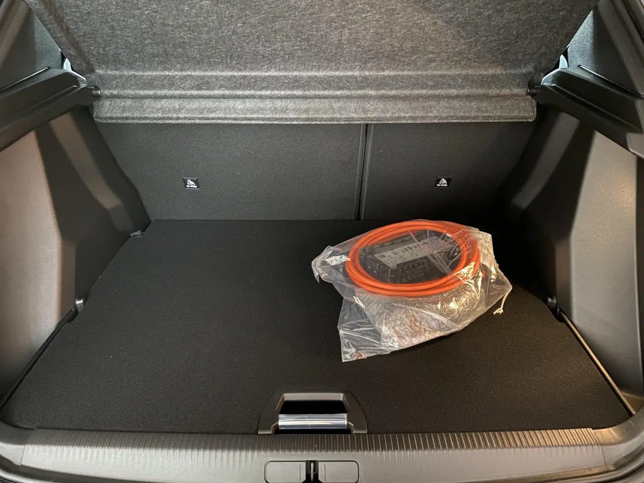 Coffre ouvert d'un Peugeot 2008 e-136 Allure Pack gris Artense avec câble de recharge électrique orange emballé.