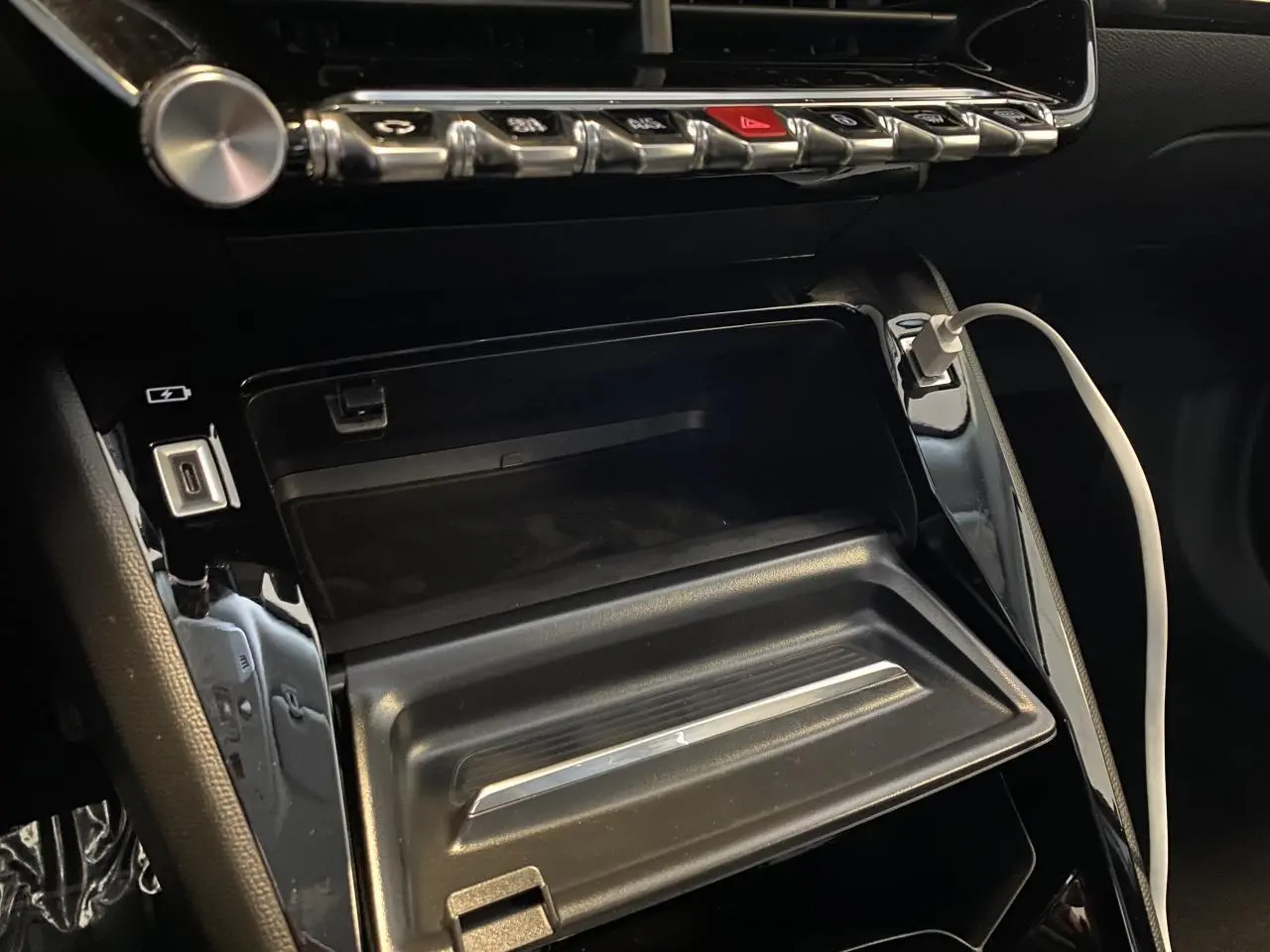 Gros plan sur la console centrale du Peugeot 2008 e-136 Allure Pack 2022 avec câble USB blanc connecté.