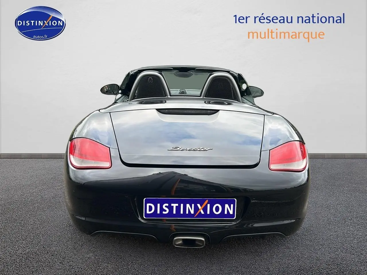 Vue arrière d'une Porsche Boxster 987 noire découvrable avec feux arrière rouges et échappement central.