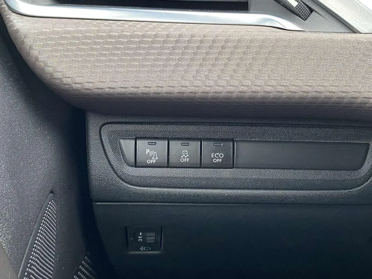 Gros plan sur les commandes de désactivation d'assistance et d'économie d'énergie dans l'habitacle d'une Peugeot 2008 blanche de 2015.