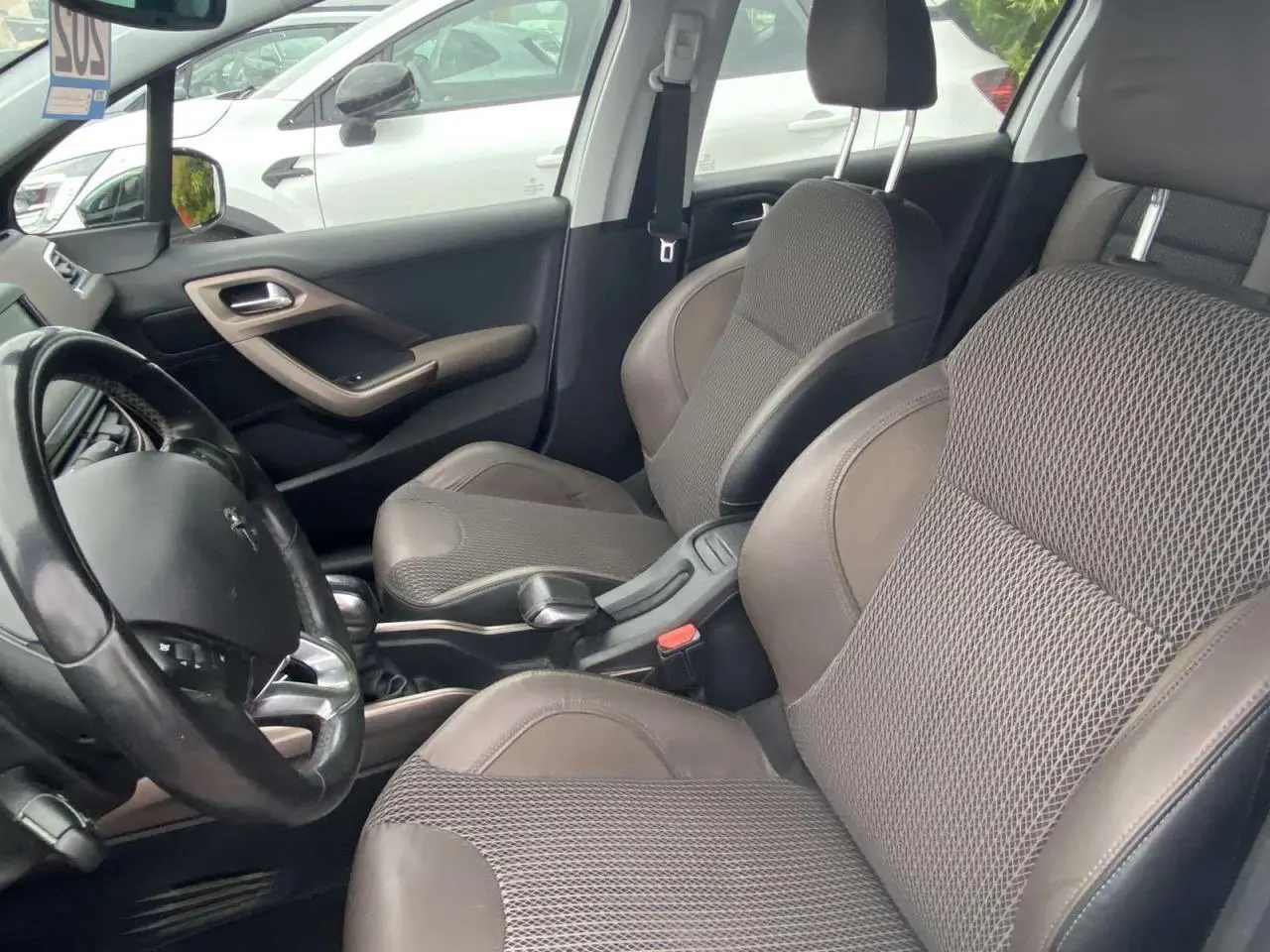 Vue intérieure côté conducteur du Peugeot 2008 blanc de 2015, avec sièges tissu et cuir gris et volant multifonction.