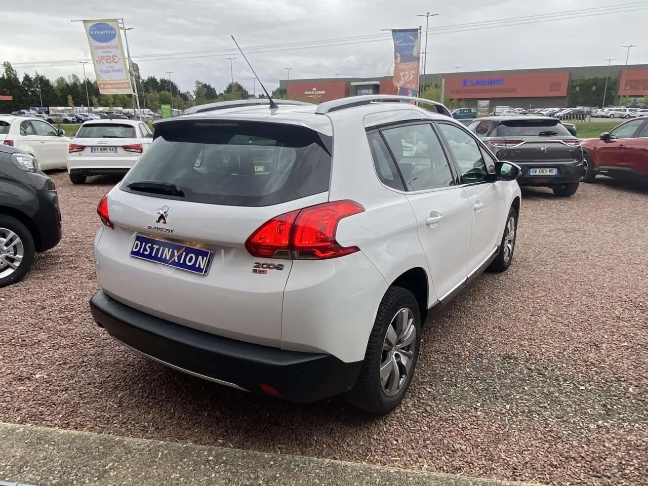 Vue 3/4 arrière droite d'un Peugeot 2008 blanc de 2015 avec logo et feux arrière distinctifs sur parking.