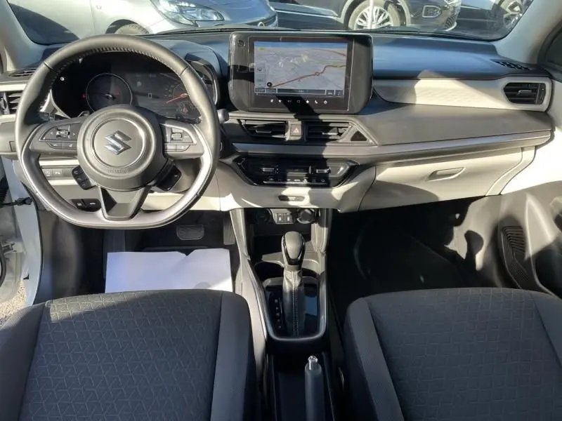 Vue intérieure avant de la Suzuki Swift blanche 2025, montrant le tableau de bord avec écran tactile et volant multifonction.