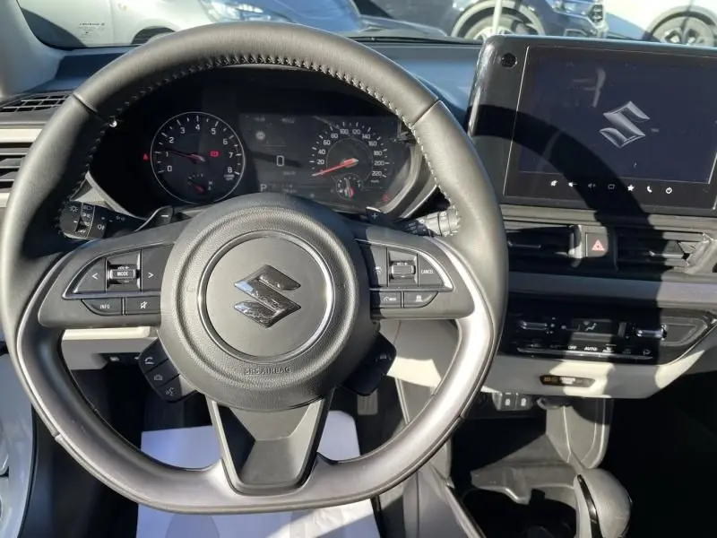 Vue intérieure centrée sur le volant de la Suzuki Swift blanche 2025 avec tableau de bord et écran tactile visible.