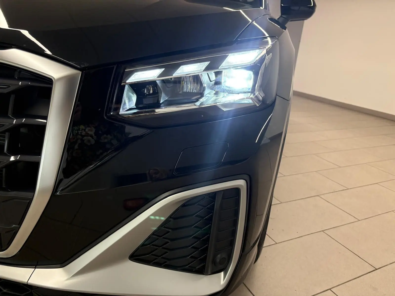 Gros plan sur le phare avant droit allumé de l’Audi Q2 35 TFSI S Line noir mythic, avec calandre et détails argentés.