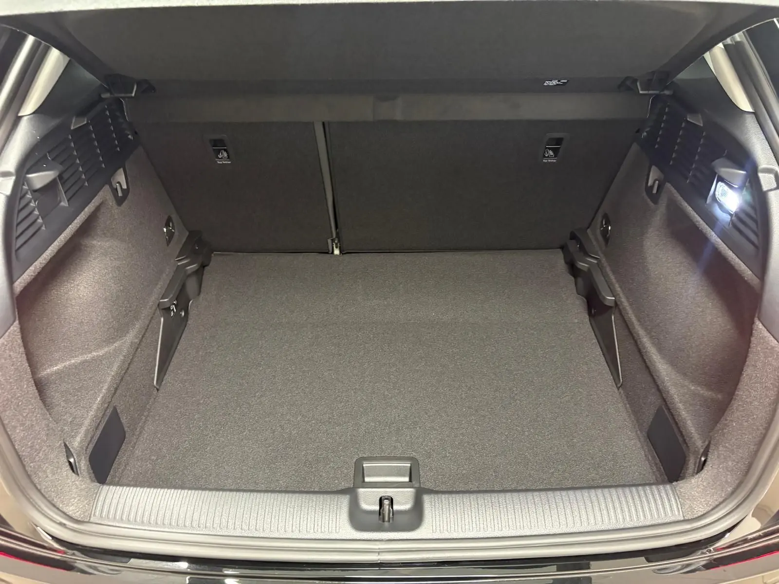 Coffre ouvert vu de l'arrière d'un Audi Q2 Noir Mythic, montrant un espace de chargement propre et bien éclairé.