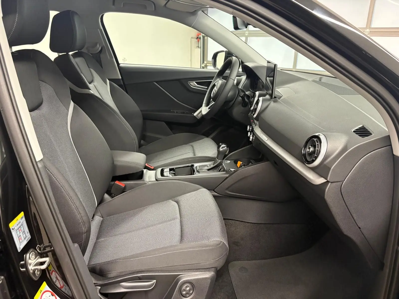 Intérieur avant droit de l’Audi Q2 35 TFSI S Line 2026 avec sièges tissu gris et tableau de bord noir.