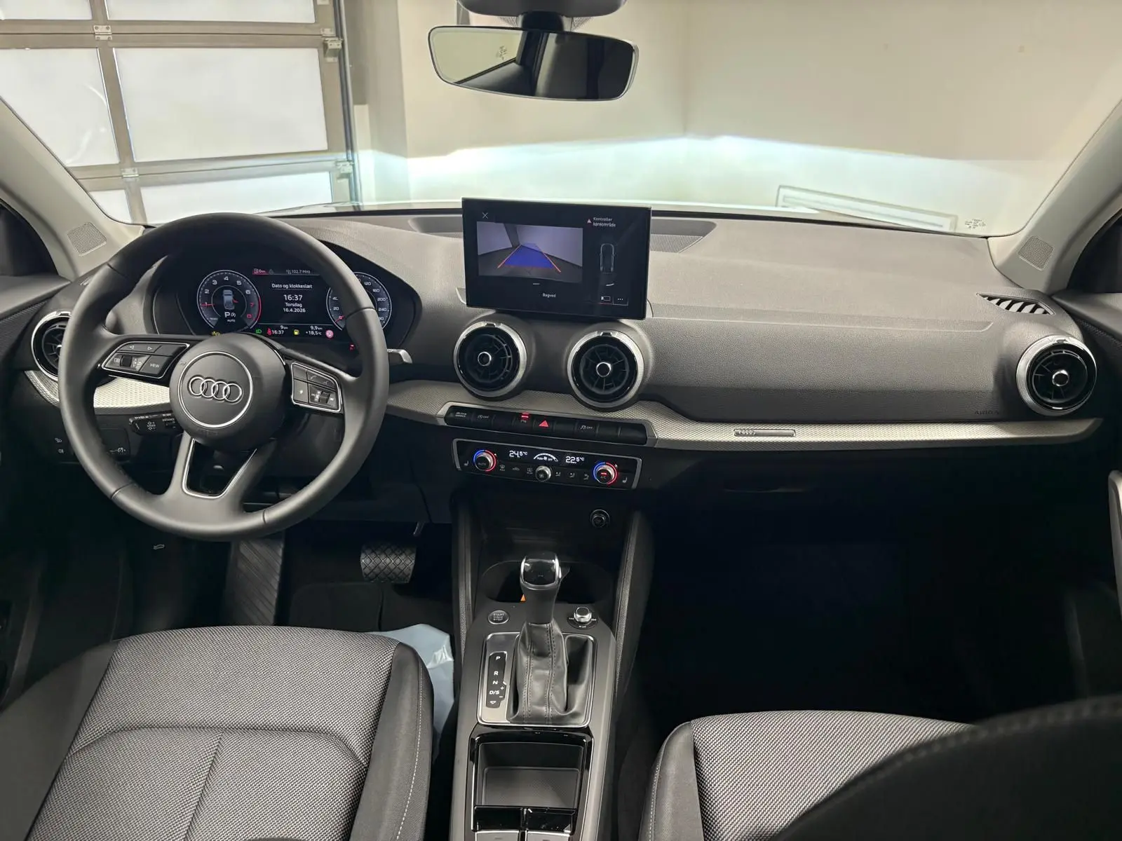 Vue intérieure de l'Audi Q2 35 TFSI S Line 2026, tableau de bord et console centrale avec écran et volant multifonctions.