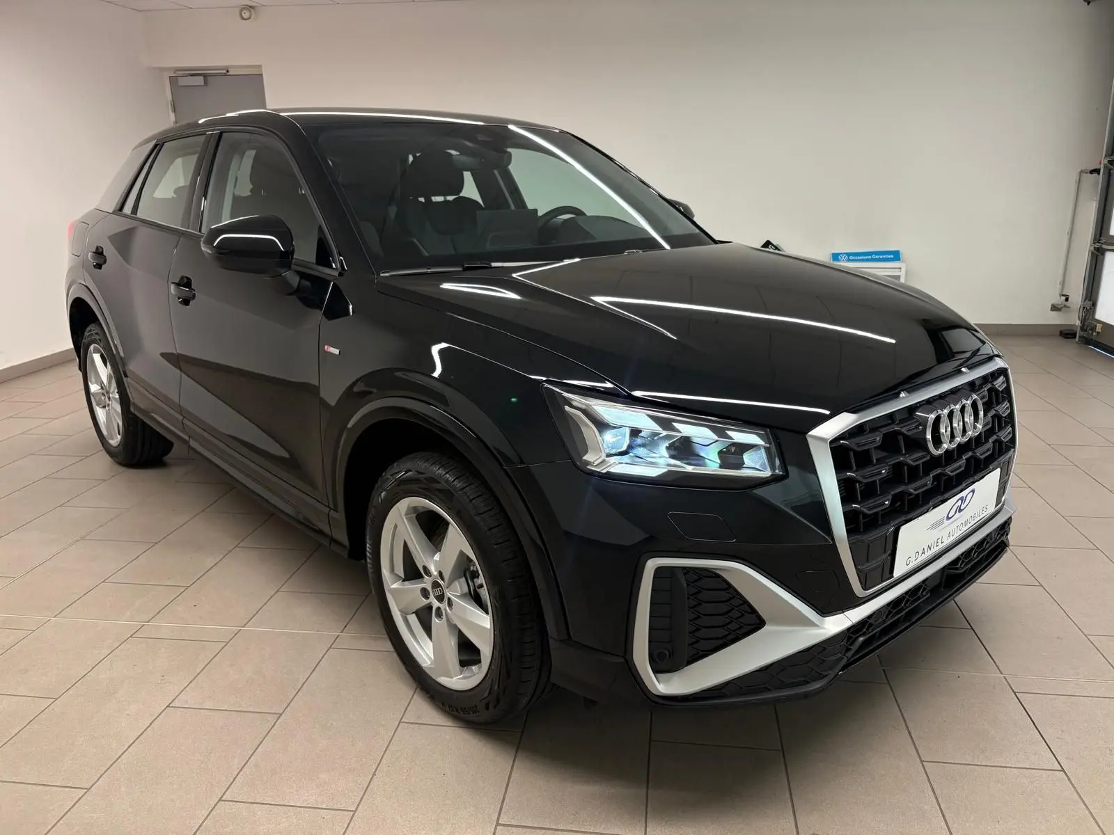 Audi Q2 35 TFSI S Line noir mythic en 3/4 avant droit, avec calandre large et feux LED allumés.
