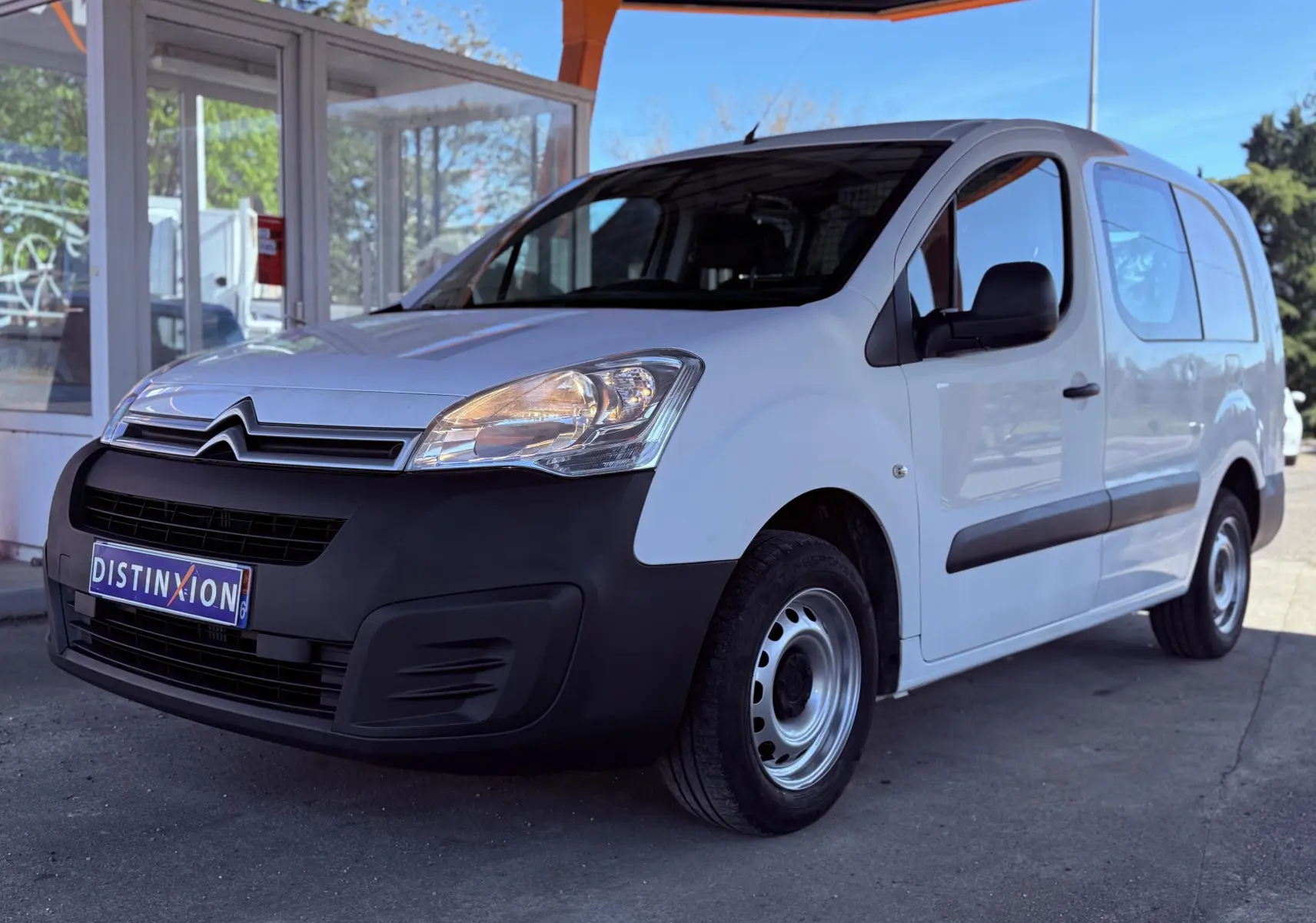 Vue 3/4 avant droite d'un Citroën Berlingo blanc avec pare-chocs noir et jantes acier sous un abri.