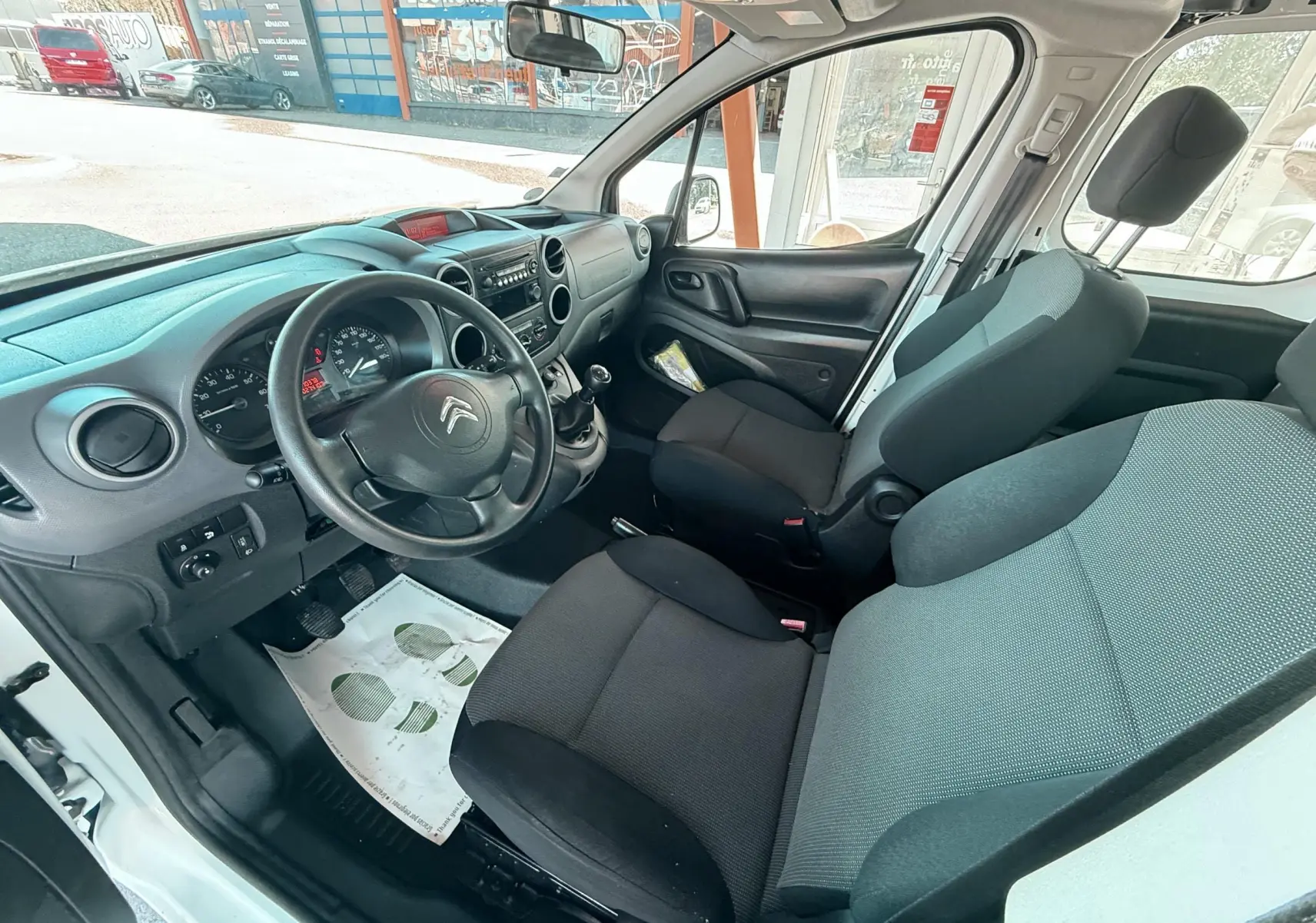 Vue intérieure côté conducteur du Citroën Berlingo blanc, montrant le volant, tableau de bord et sièges en tissu noir.