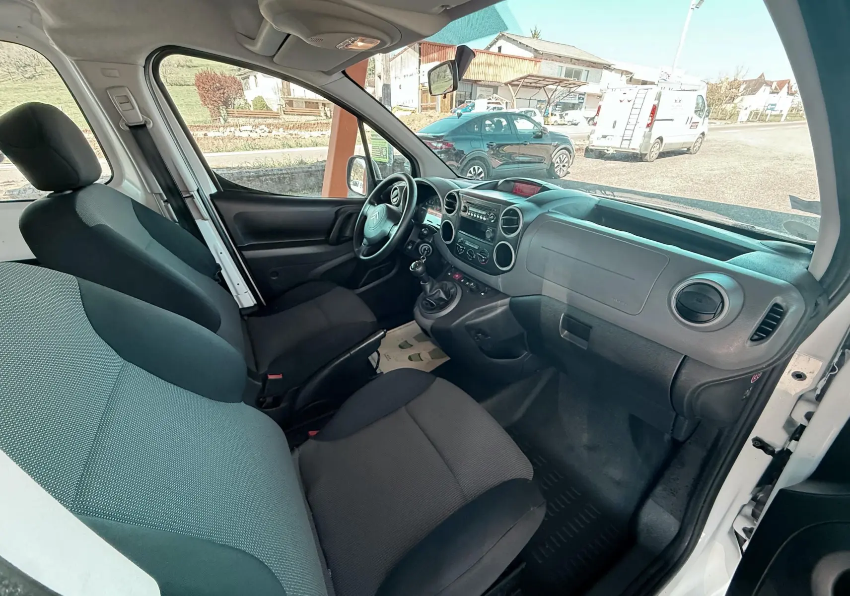 Vue intérieure côté conducteur du Citroën Berlingo blanc 2017, montrant le tableau de bord et les sièges en tissu noir.