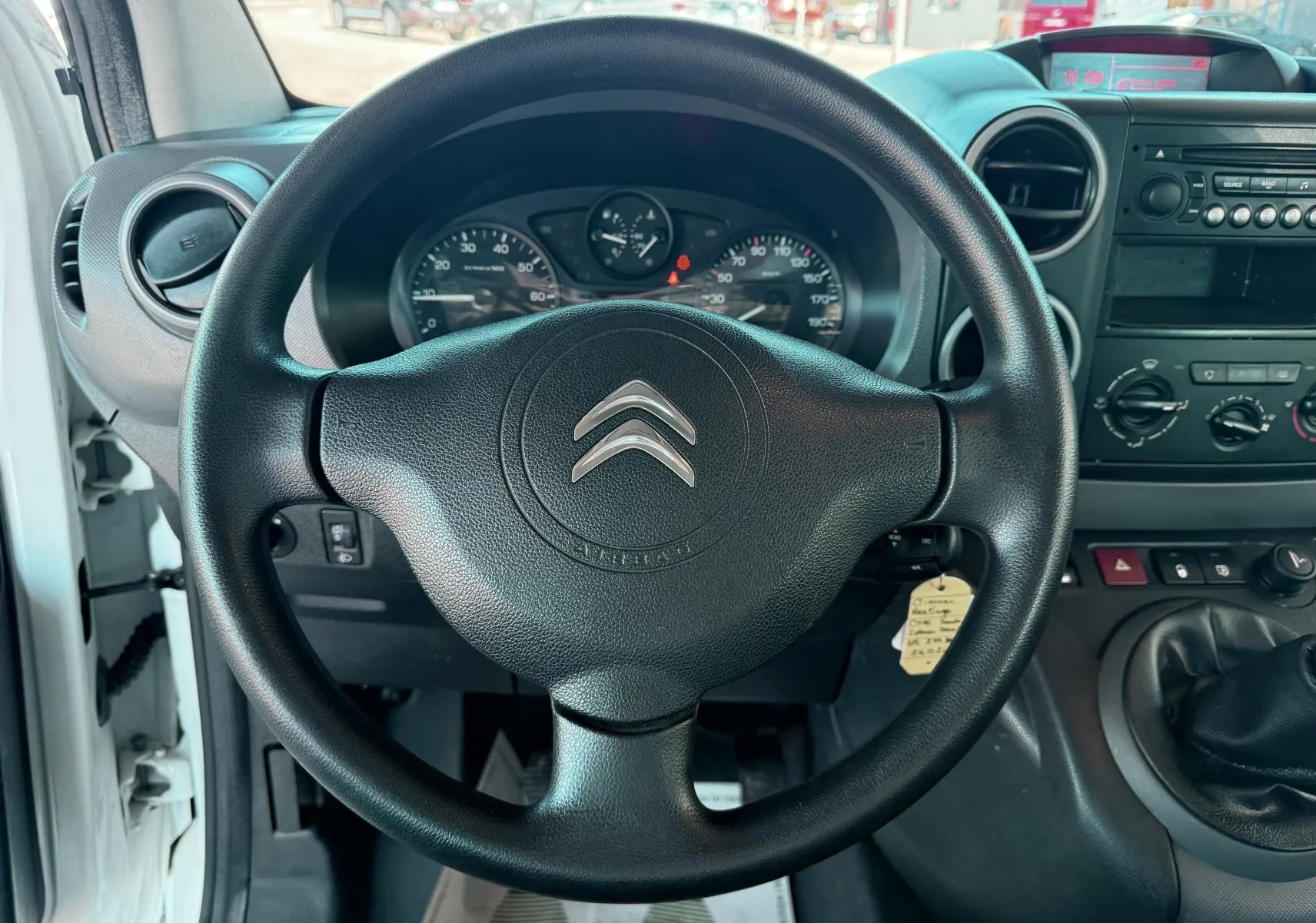 Vue intérieure centrée sur le volant noir Citroën d'un Berlingo blanc, avec tableau de bord et levier de vitesses manuelle visibles.