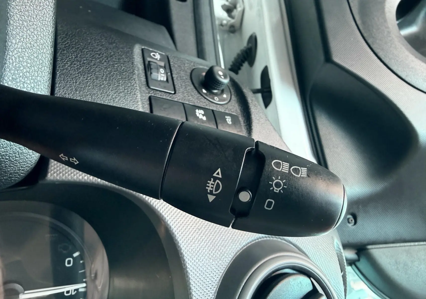 Gros plan sur la manette de clignotants et commandes d’éclairage du tableau de bord d’un Citroën Berlingo blanc, côté conducteur.