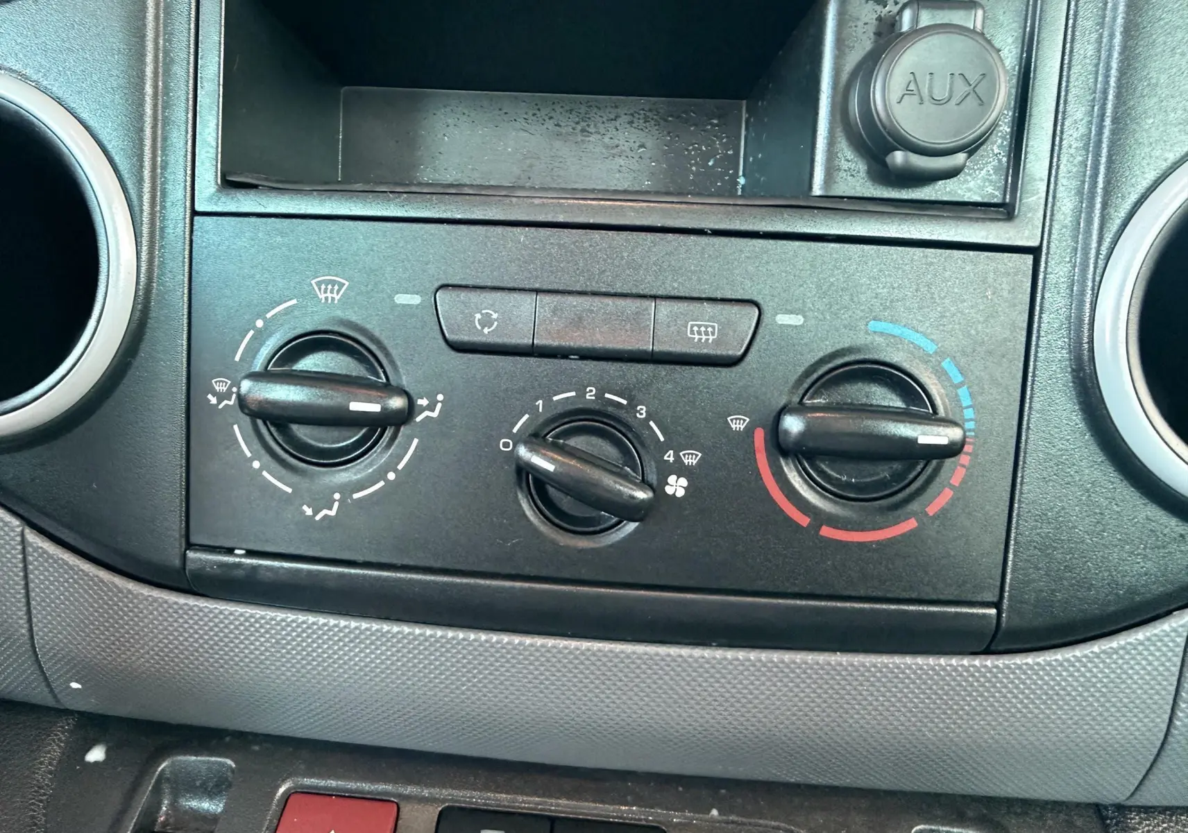 Gros plan sur la console centrale noire du Citroën Berlingo 2017, montrant les commandes de climatisation et prise AUX.