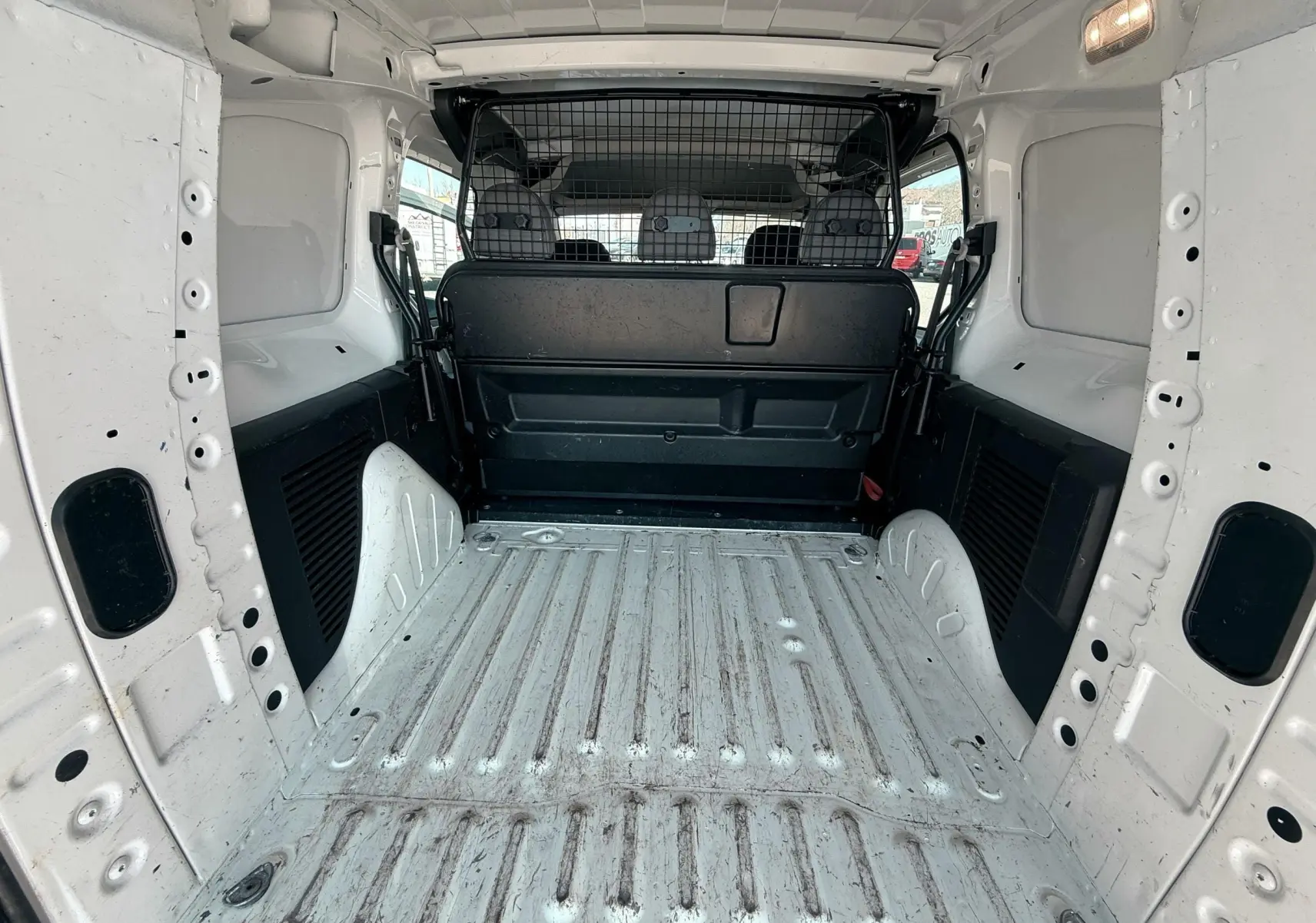 Vue intérieure arrière du coffre blanc du Citroën Berlingo 1.6 HDI 100 Confort avec séparation grillagée noire.