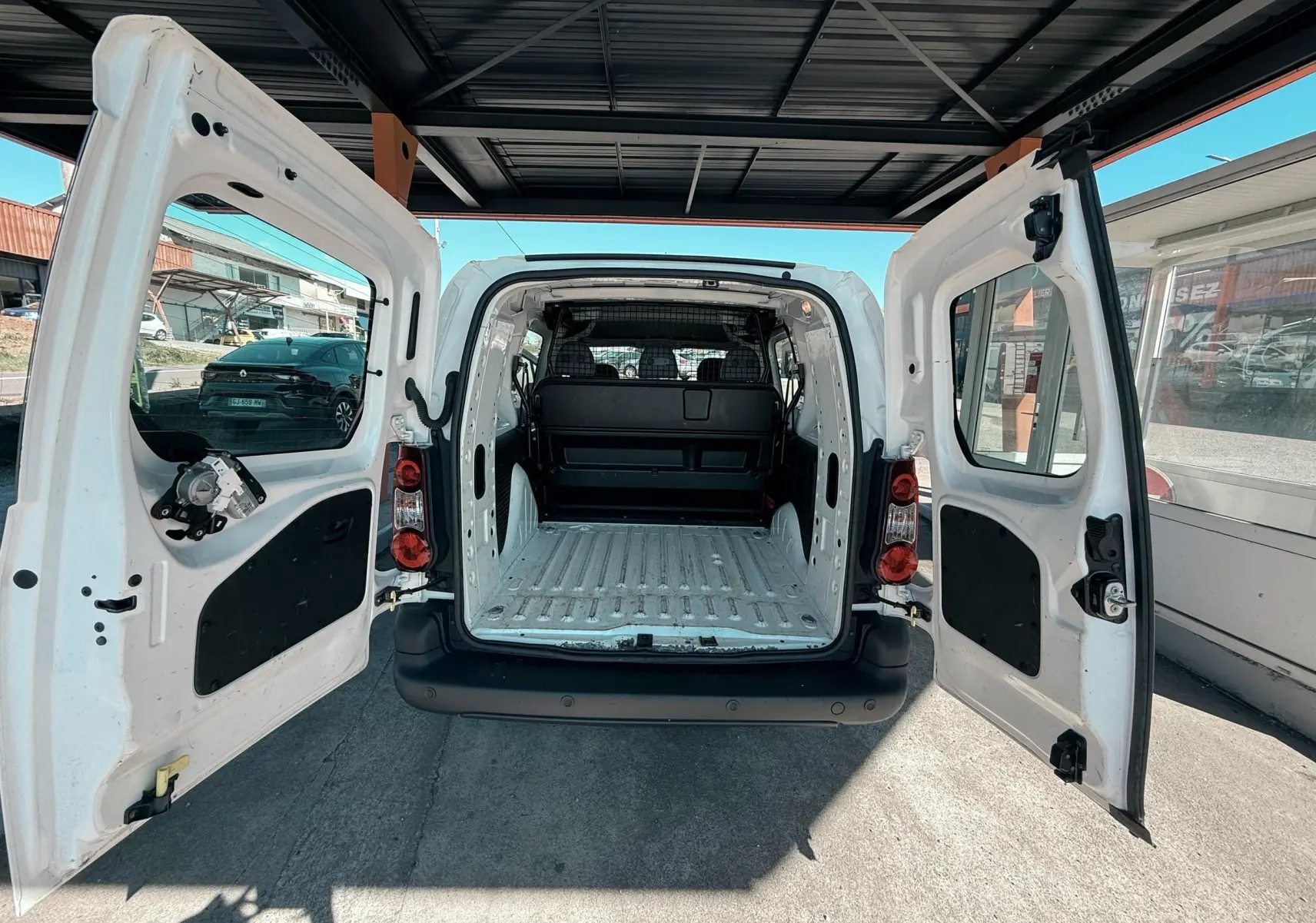 Vue arrière du Citroën Berlingo blanc 2017 avec portes ouvertes montrant l’espace de chargement vide et la cloison de séparation.