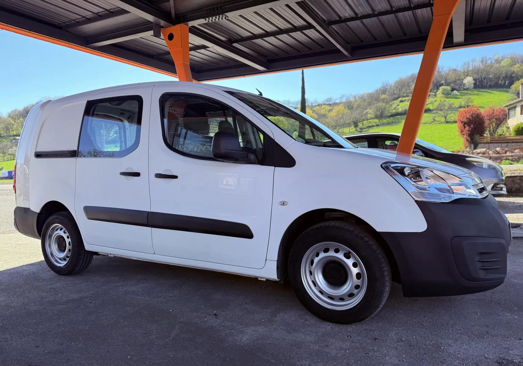 Vue de profil droit du Citroën Berlingo blanc 2017 avec pare-chocs noirs et jantes acier sous abri.